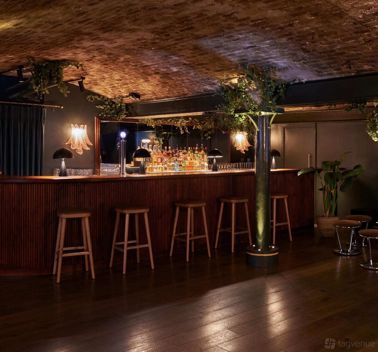 A function room with a brick vaulted ceiling, hanging greenery, and a wooden bar with stools at Casa do Frango - Mayfair.