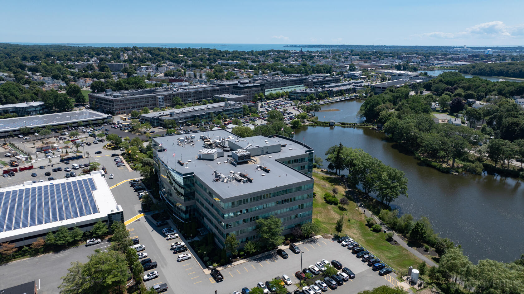 An office building with large windows, adjacent to a river and surrounded by parking at Workspace Beverly.