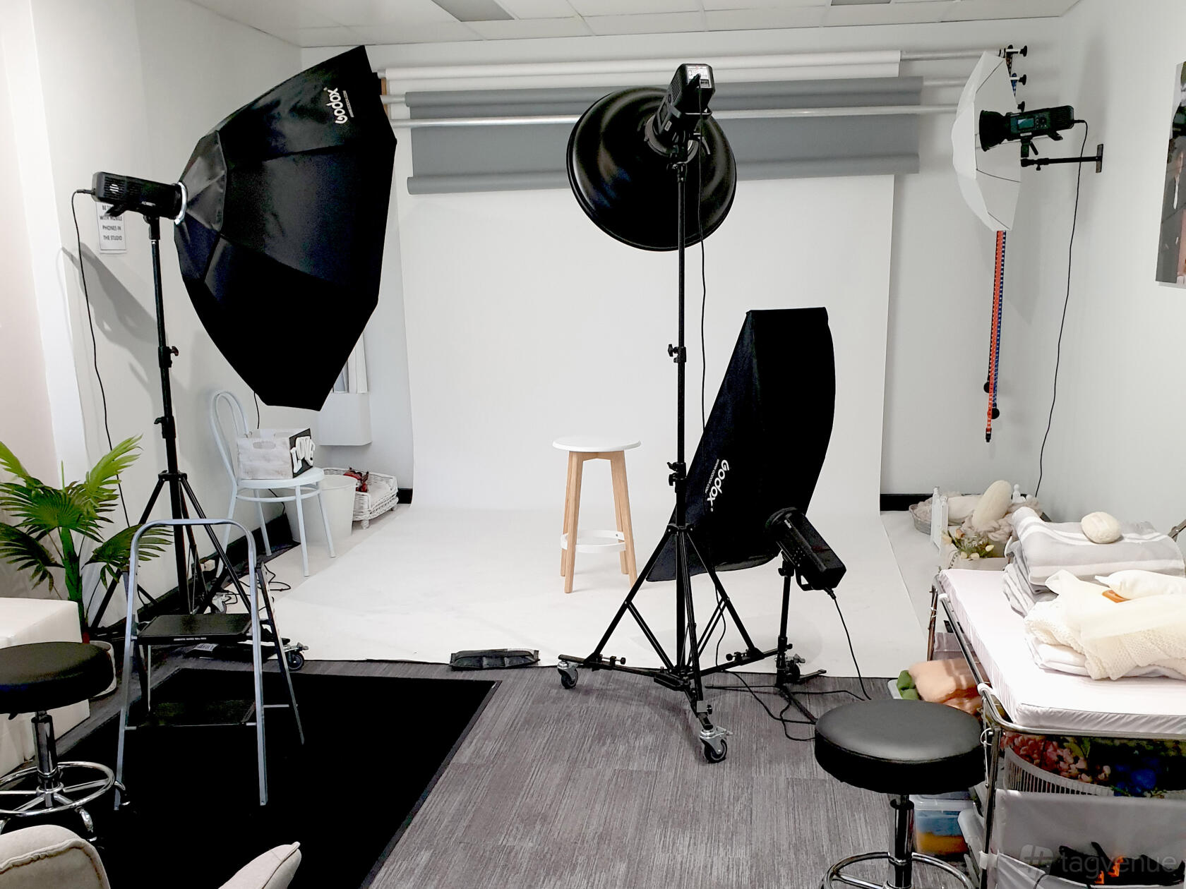 A photo studio with a white backdrop, professional lighting equipment, and a wooden stool at St Leonards Studio.
