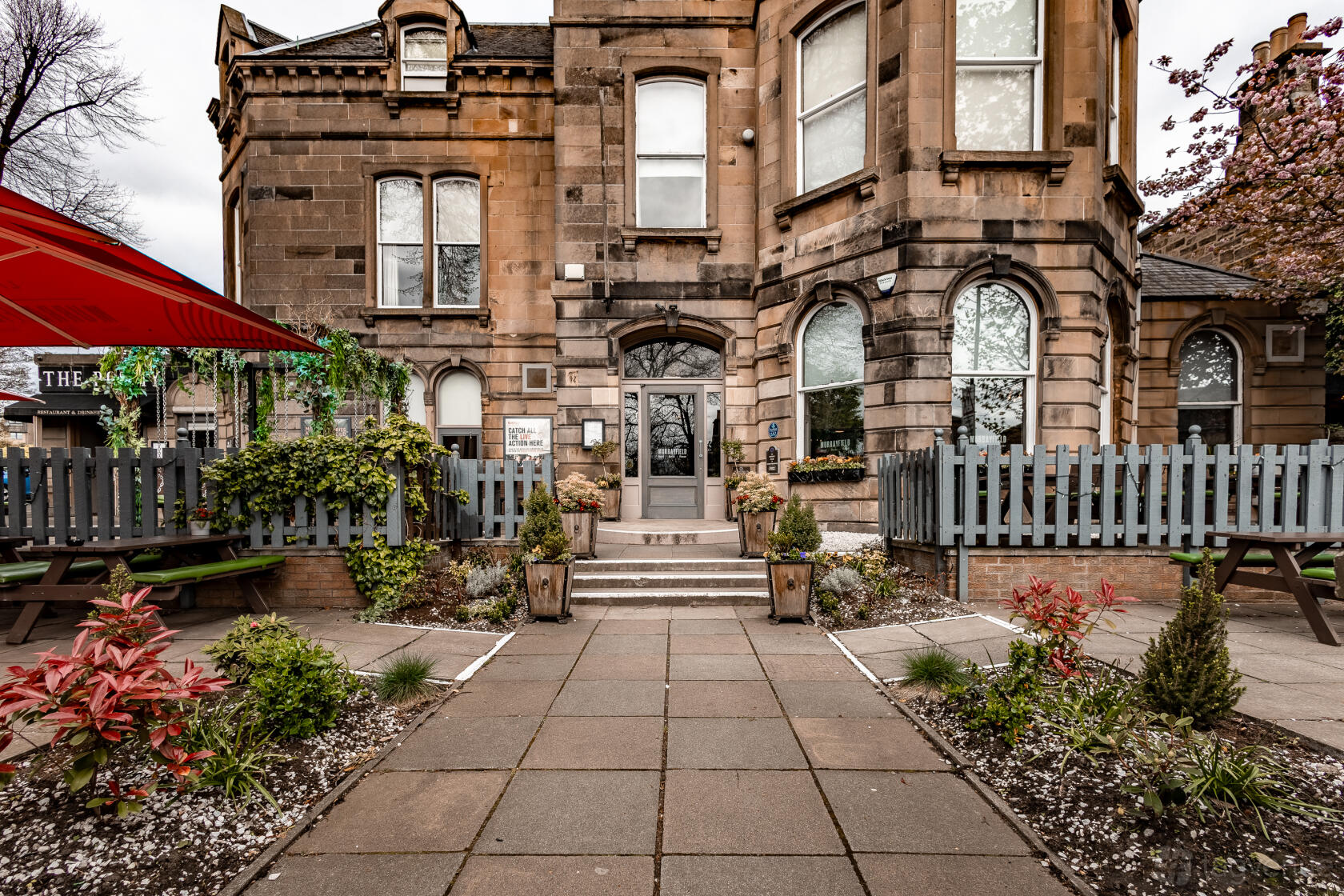 A hotel with a stone facade, arched windows, a central entrance, and surrounding landscaped gardens at The Murrayfield Hotel.