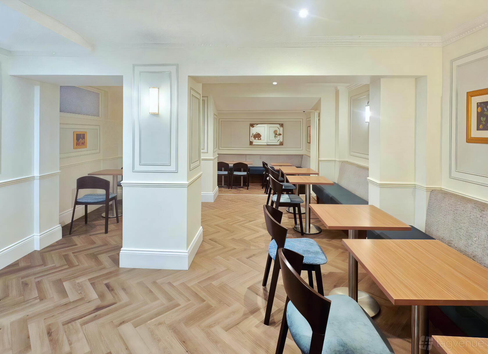 A hotel dining room with wood herringbone flooring, light walls, wall sconces, and small tables at Princes Square Hotel.