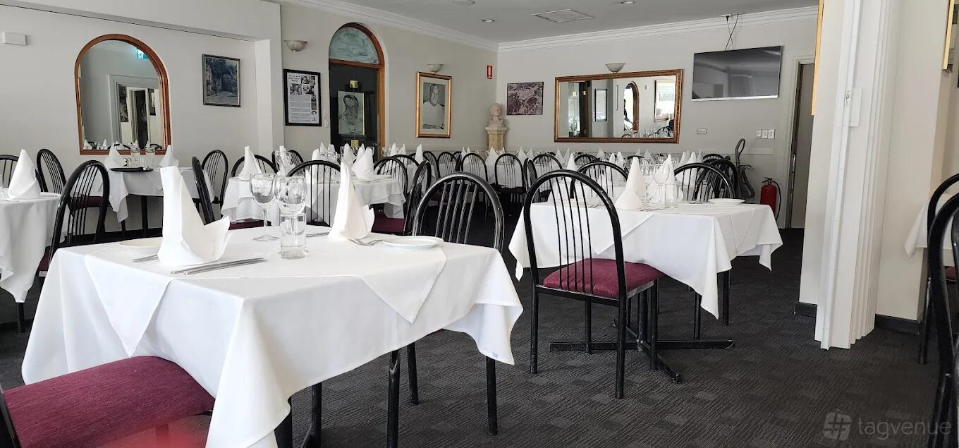 A restaurant with tables draped in white linens, folded napkins, and dark wooden chairs at Buonasera.