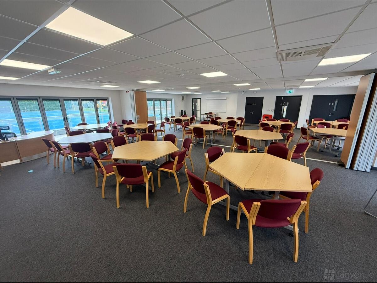 An event space with hexagonal wooden tables, red cushioned chairs, and large windows at King Edward VI Five Ways School.