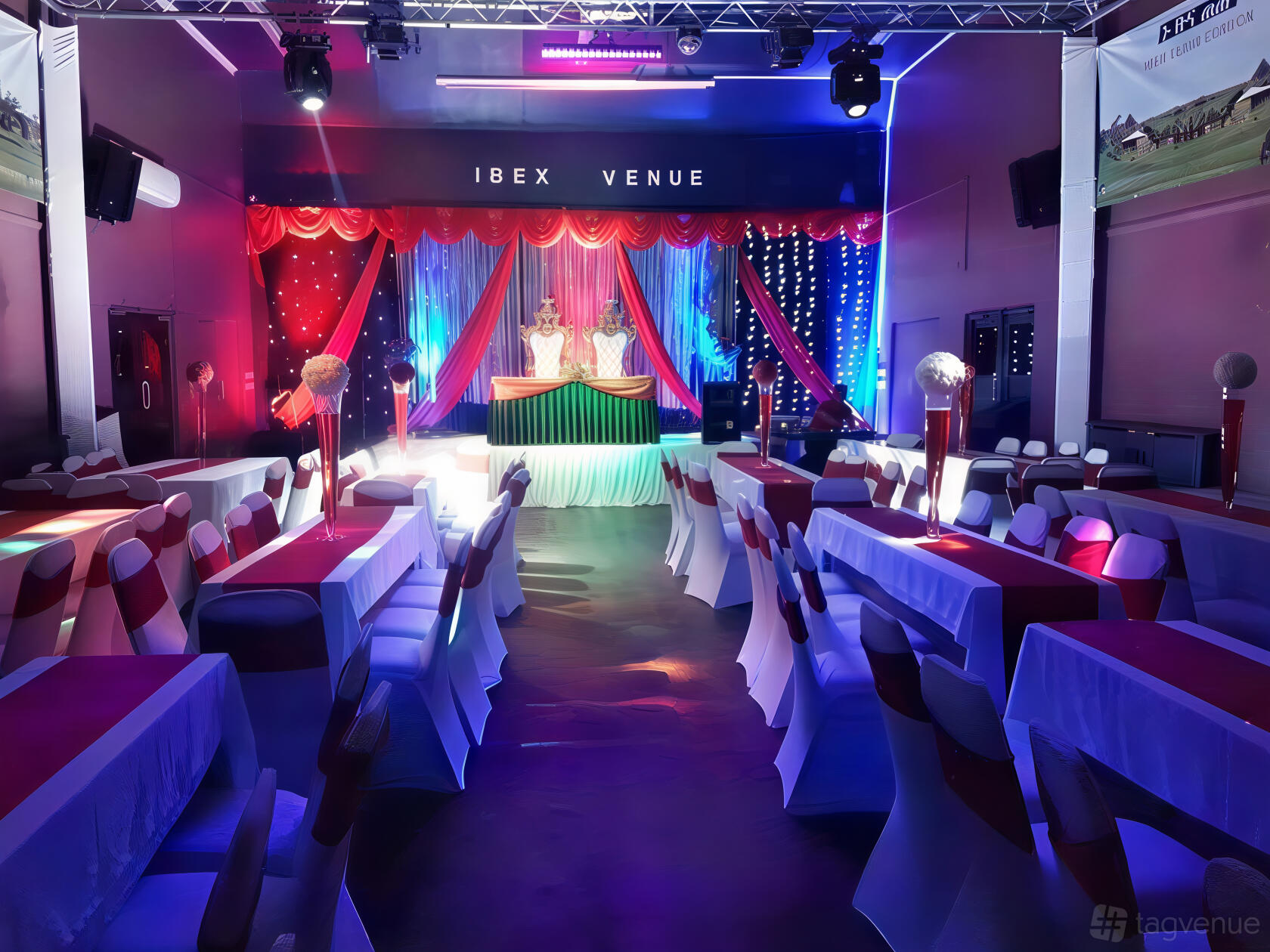 An event venue with banquet tables covered in white and red linens and a stage draped with red curtains at Ibex Venue.