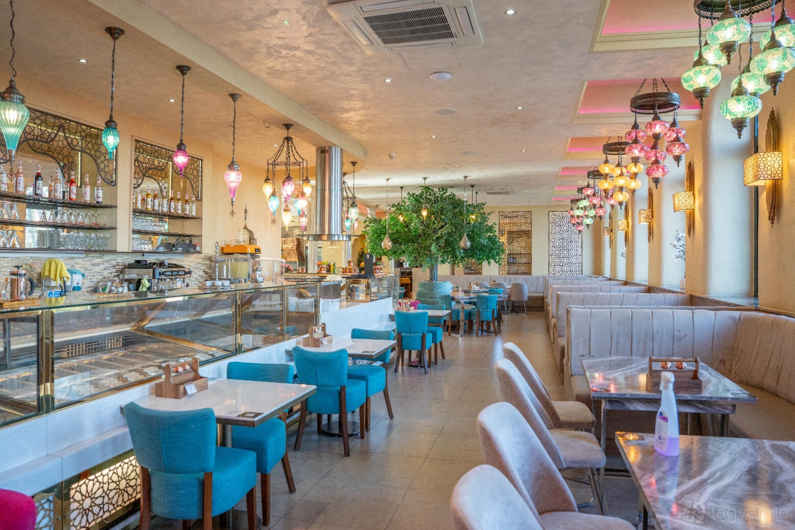 A restaurant dining area with colorful pendant lamps, turquoise and beige chairs, and marble tables at Mezza Restaurant.