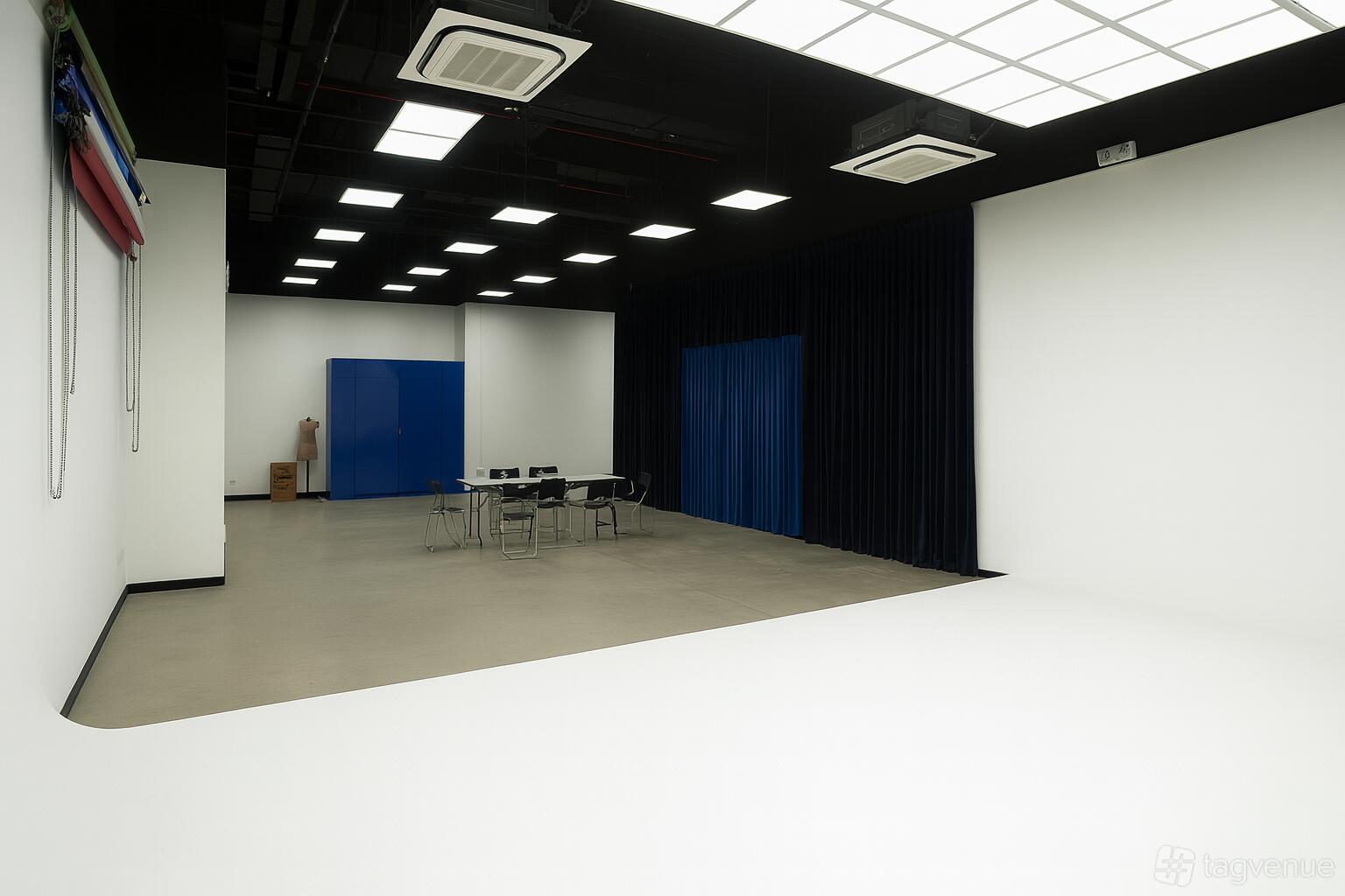 A photo studio with a white cyclorama wall, seamless paper backdrops, and folding chairs at The Studio @ SG.