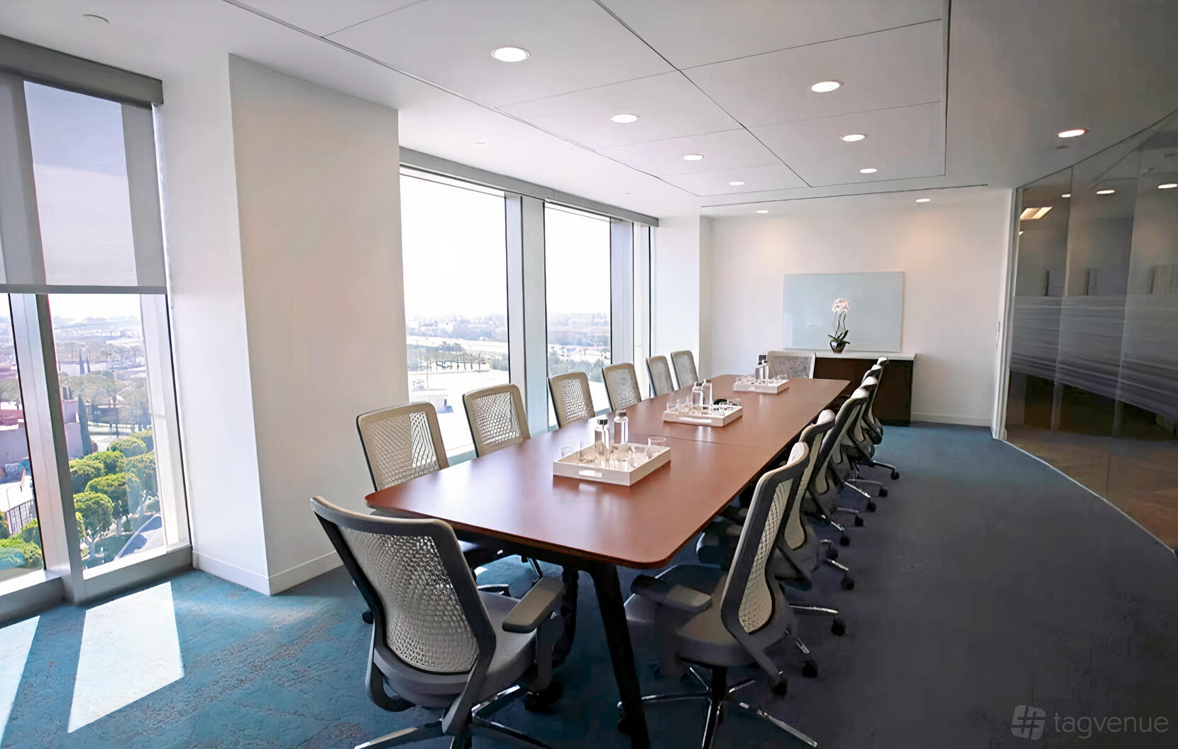 A boardroom with floor-to-ceiling windows, ergonomic chairs, and a long conference table at Regus – Belfast City Centre.