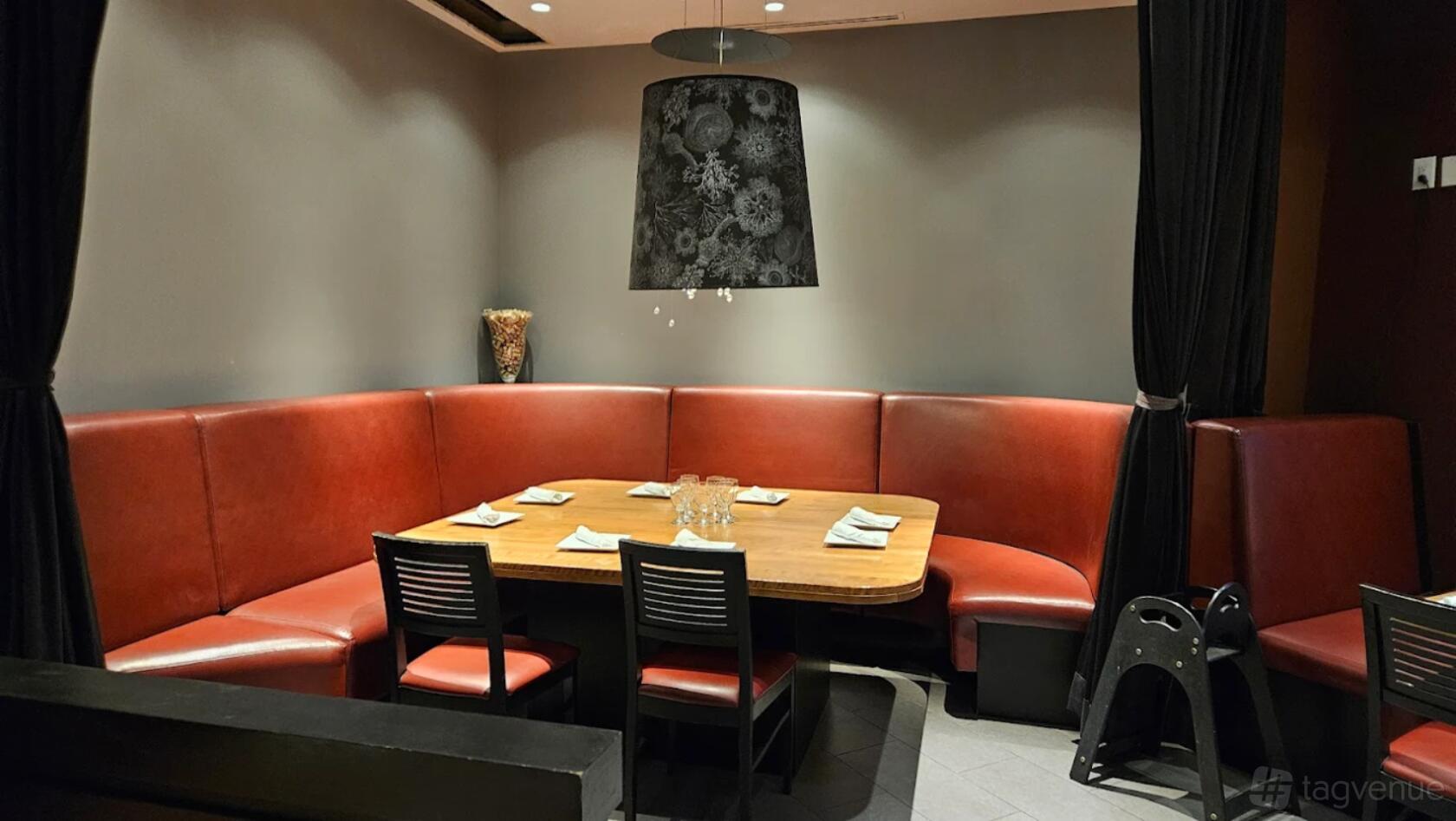 A restaurant with red leather banquette seating, a wooden table set with napkins, and dim pendant lighting at Desi Pakwan.