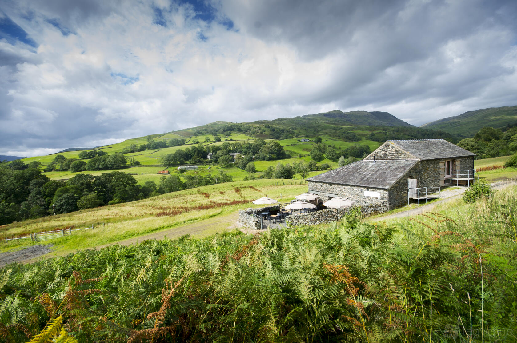 A rustic barn with stone walls and outdoor seating, set amid rolling green hills at Grove Barn.