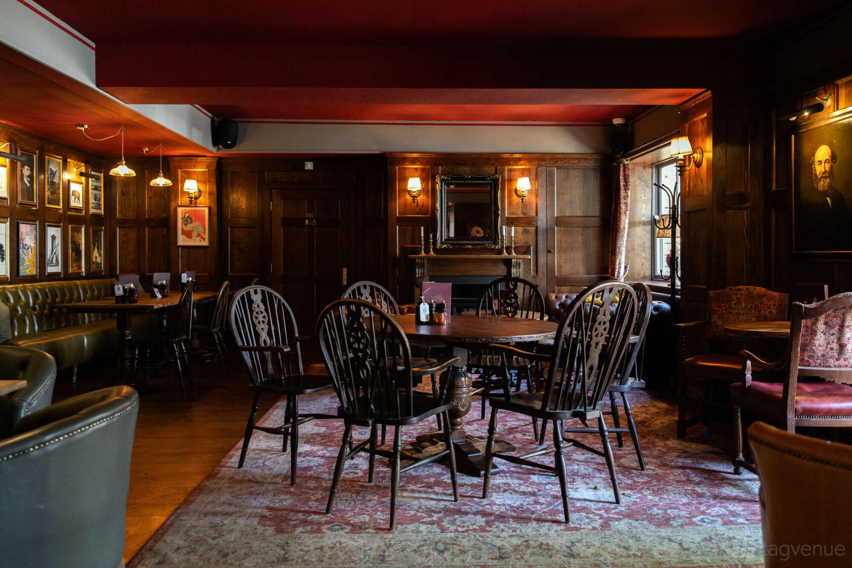 An event space in a pub with wood-paneled walls, framed portraits, and a large rug with wooden chairs at The Leather Bottle.