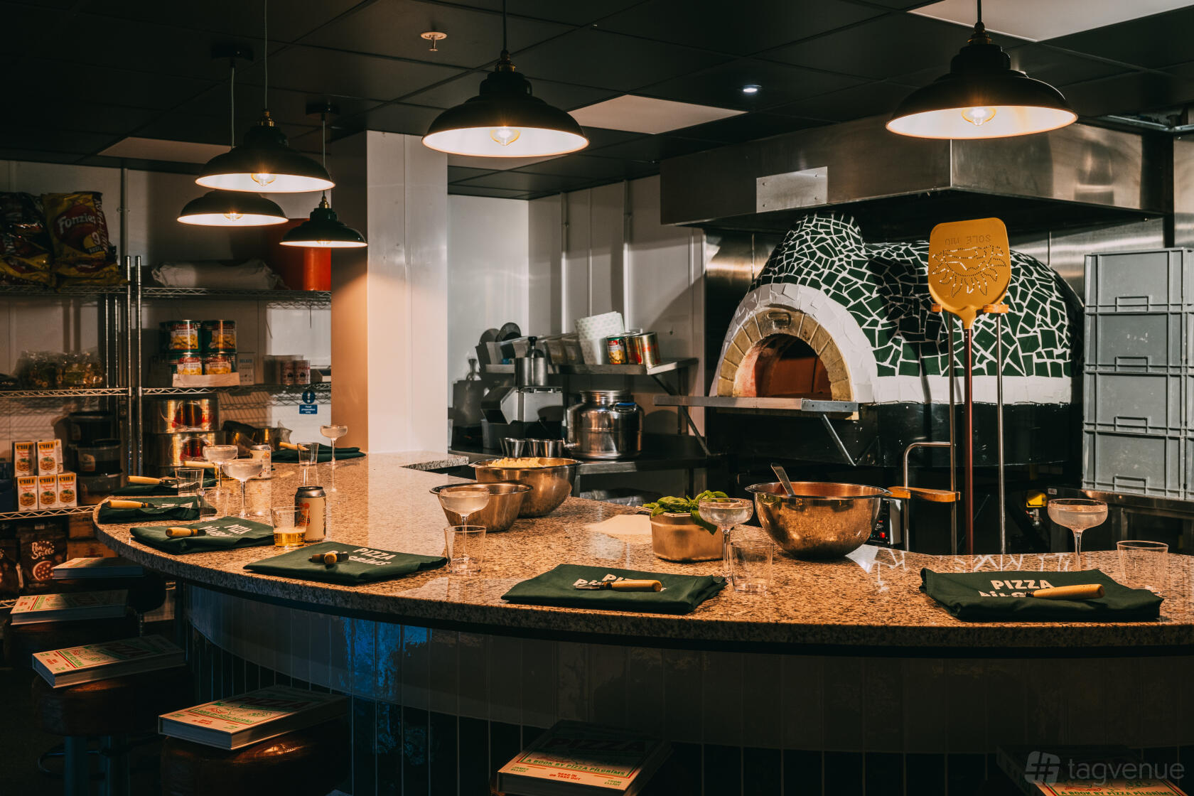 A restaurant kitchen with a marble countertop, pizza oven with mosaic tiles, and pizza-making stations at Pizza Pilgrims Canary Wharf.