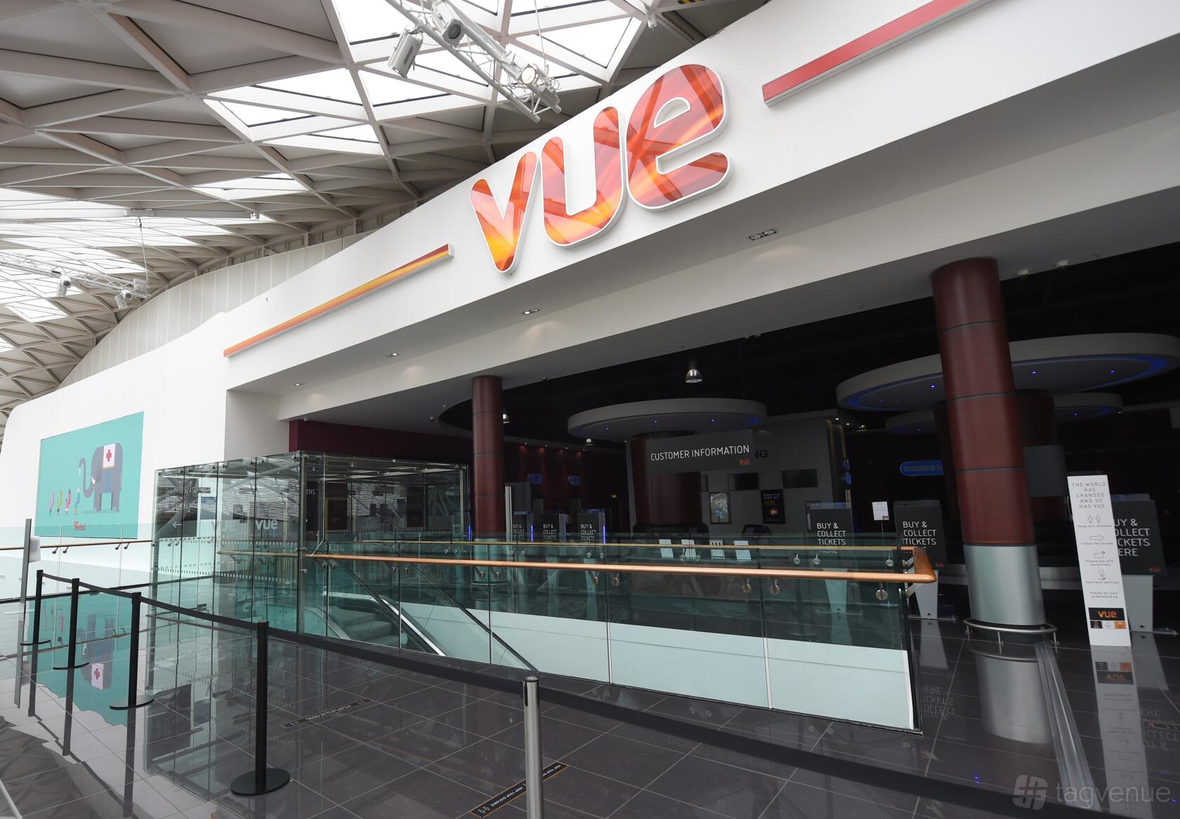 A cinema entrance with glass railings, digital screens, and a large orange Vue sign at Vue Westfield London (White City).