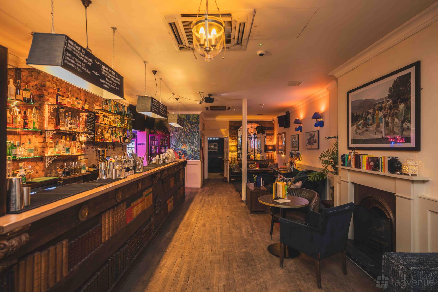 A cocktail bar with exposed brick walls, a long wooden counter, and cozy seating at The Little Blue Door.