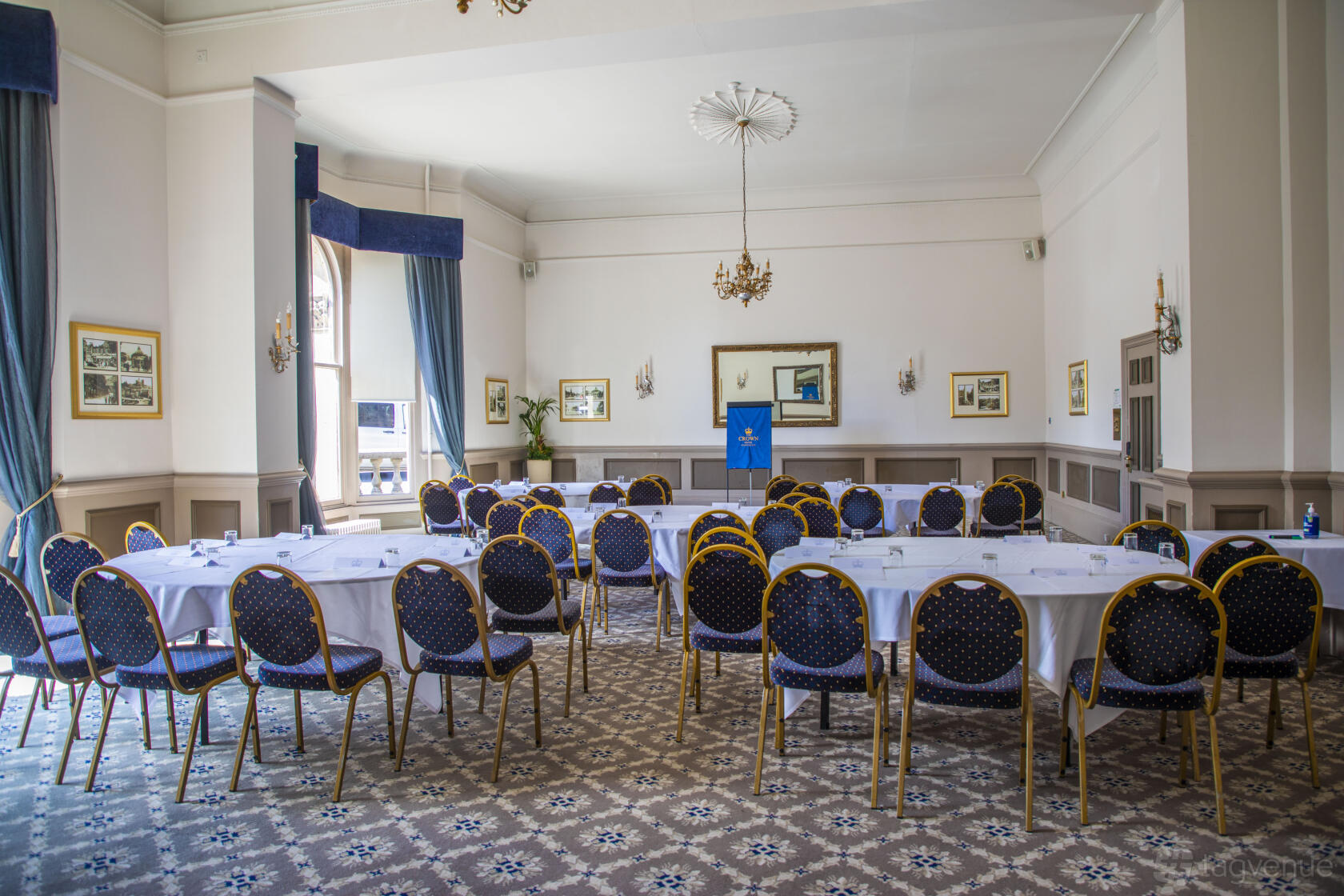 An event space with patterned carpet, round-backed chairs, chandeliers, and tall windows at The Crown Hotel Harrogate