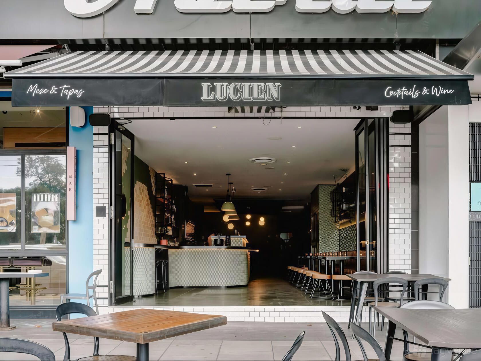 A restaurant with a black and white striped awning, open facade, and indoor bar seating at Lucien Bar.