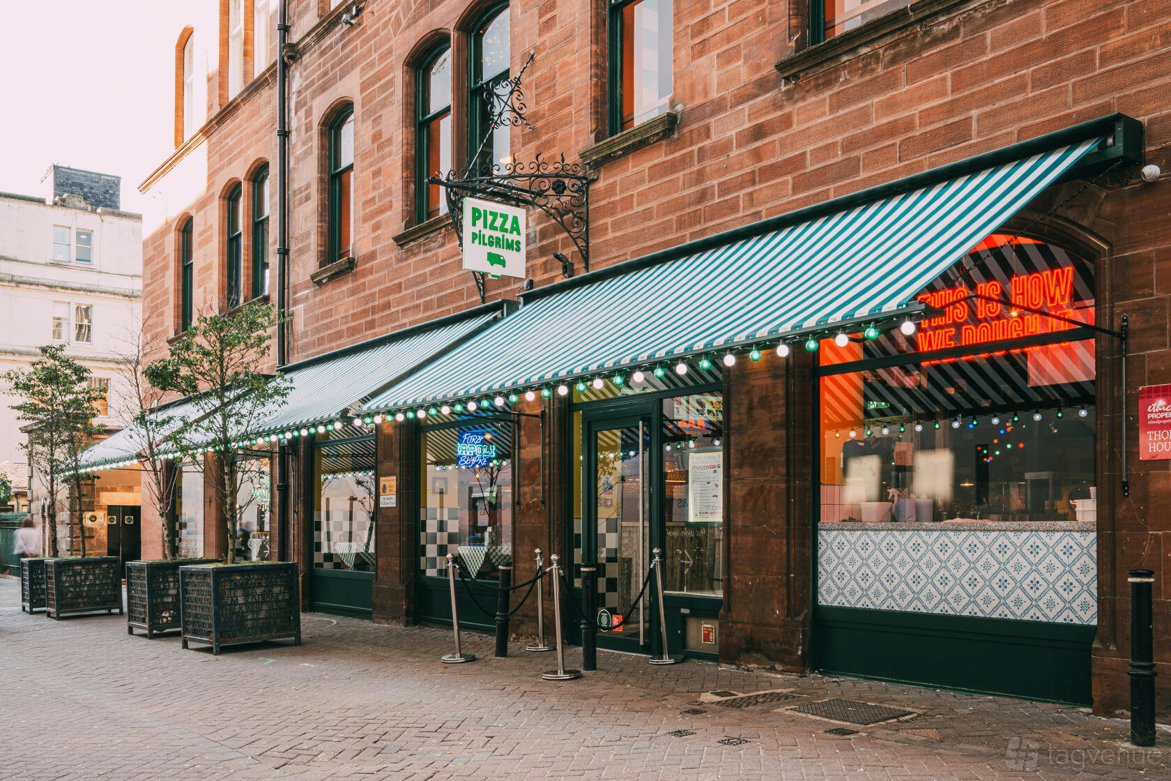 A restaurant with green-striped awnings, large windows, and outdoor planters at Pizza Pilgrims Edinburgh.