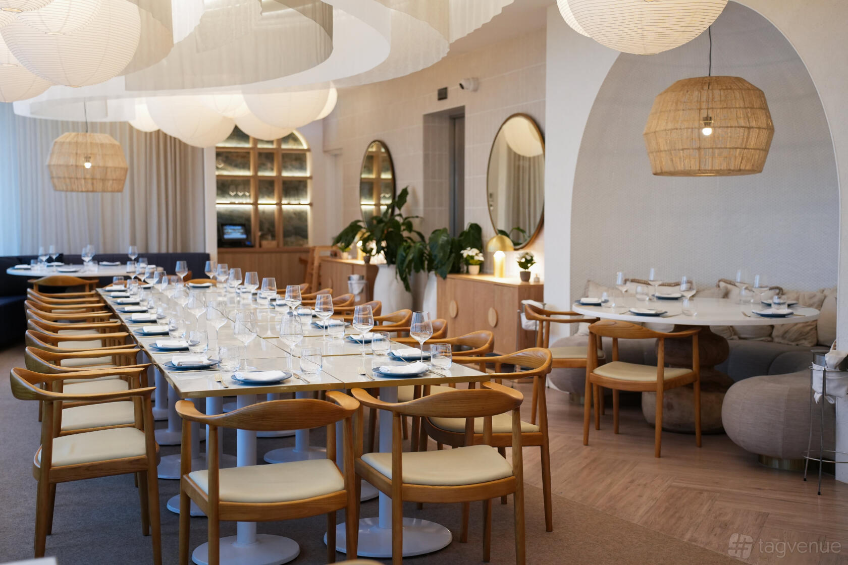 A dining room with a long marble table, wooden chairs, globe pendant lights, and round mirrors at Coast Beach Bar & Kitchen.