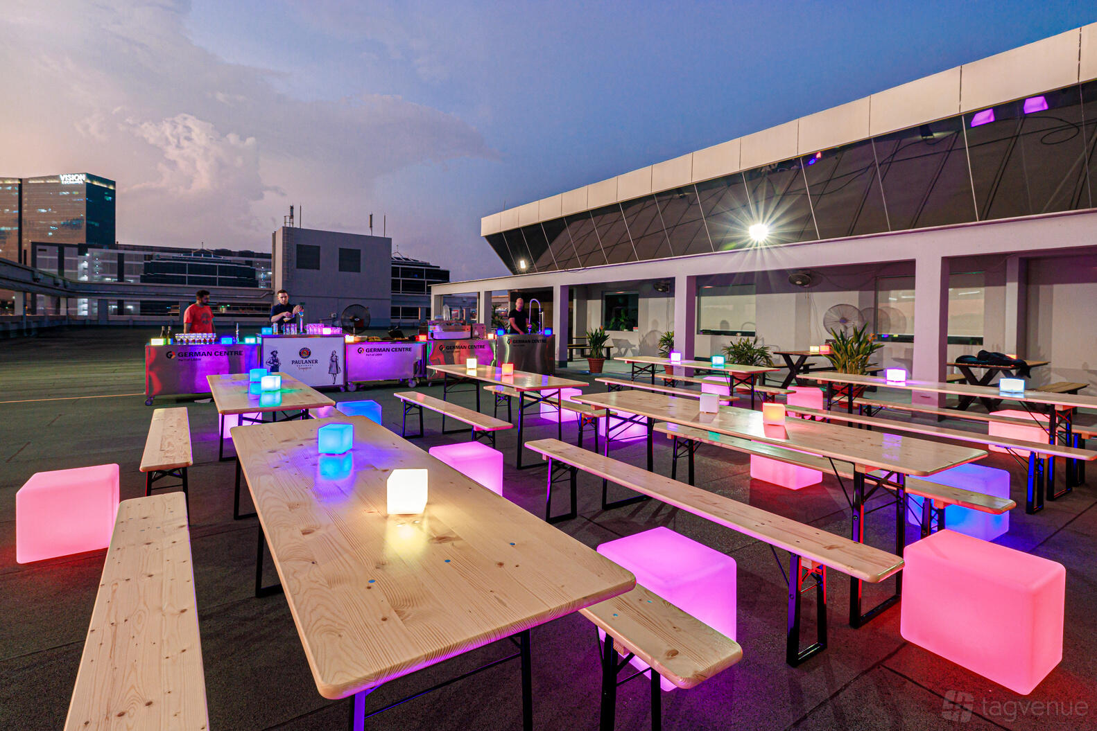A rooftop venue with long wooden tables, glowing cube seats, and city views at German Centre Singapore.
