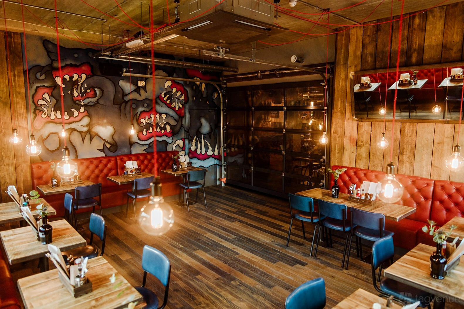 An upstairs event area with red tufted bench seating, wooden tables, and hanging pendant lights at BrewDog Edinburgh Lothian Road.
