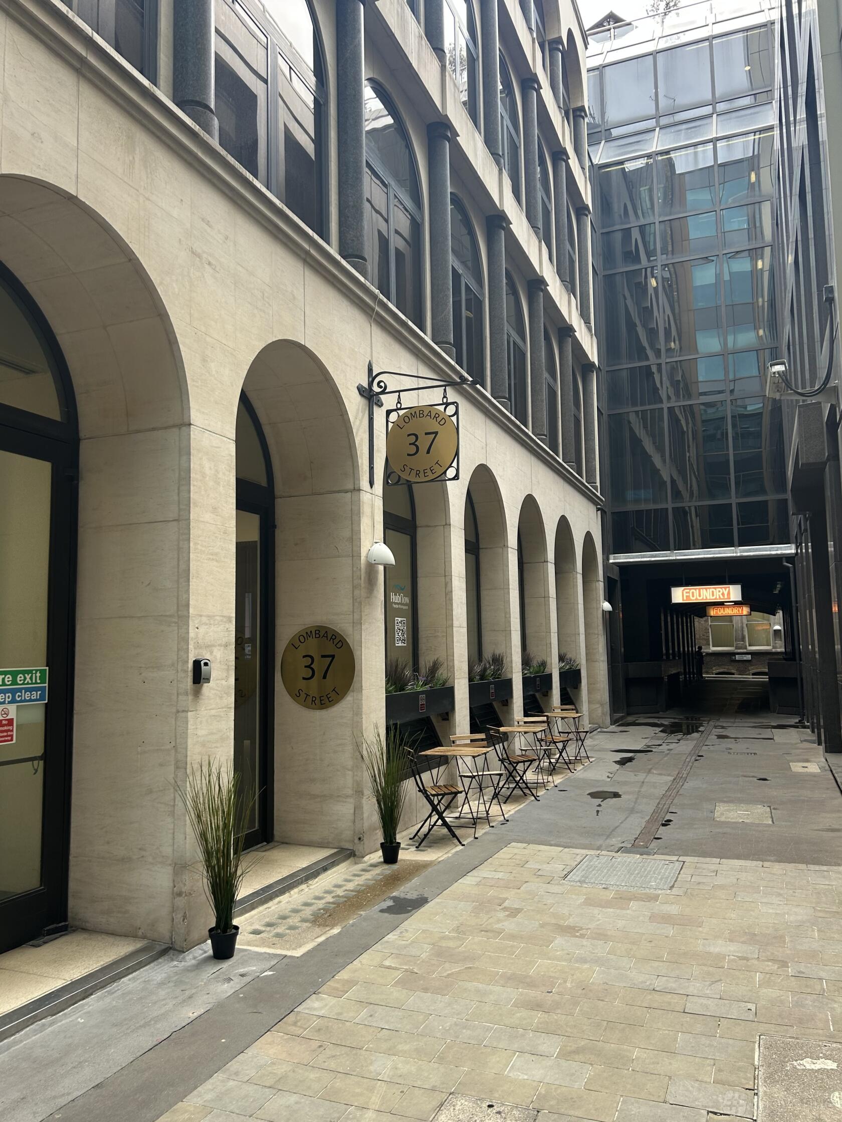 A coworking space with arched doorways, outdoor cafe tables, and potted plants at Hubflow Ltd.