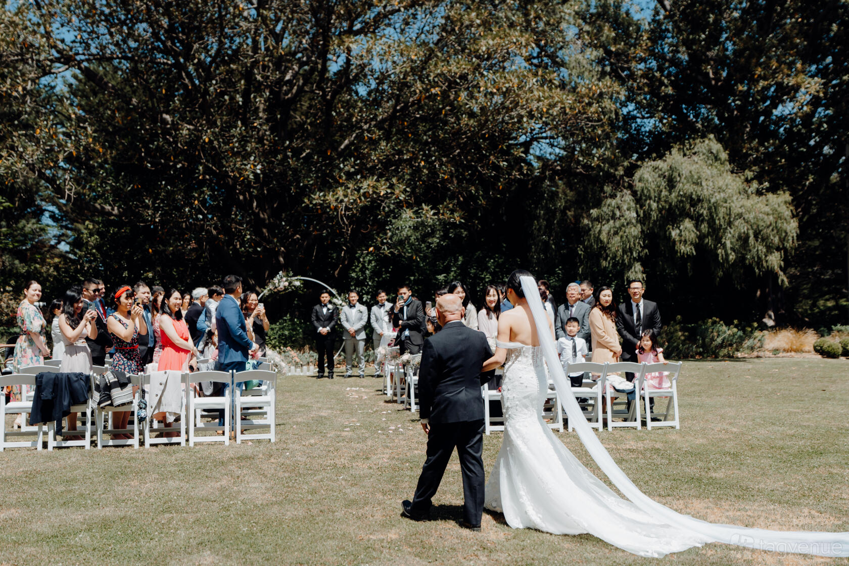 An outdoor space with rows of white chairs on a lawn under large trees at Como House and Garden.