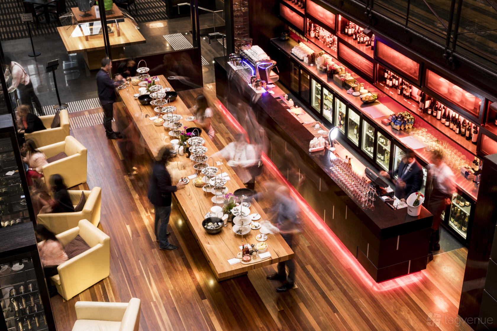 A hotel lounge with a long wooden communal table, cushioned armchairs, and a backlit bar at InterContinental Melbourne.