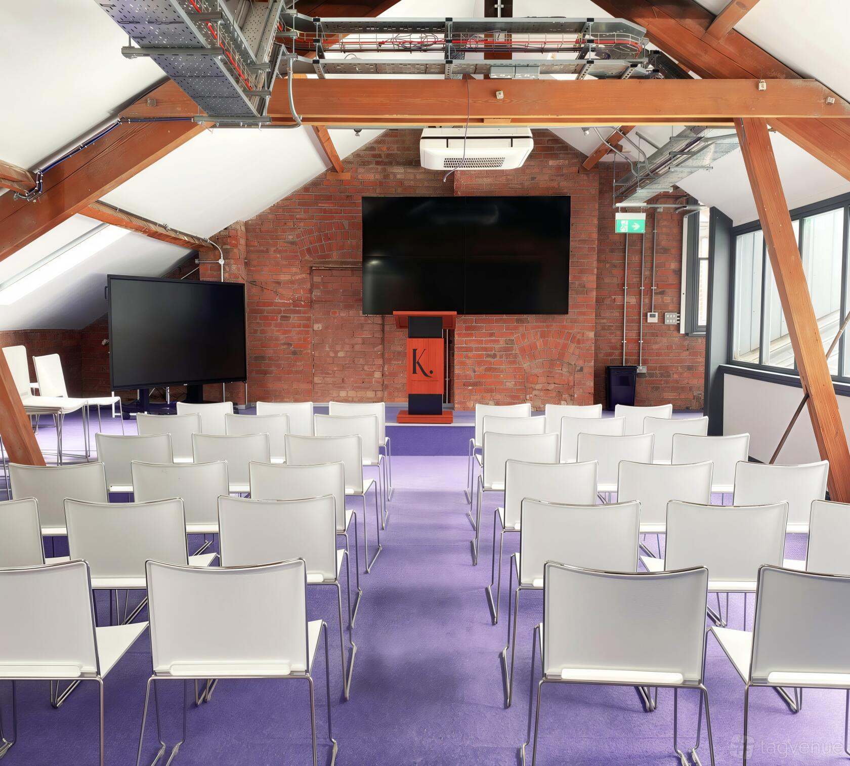 A classroom with white chairs arranged in rows facing a podium and large screen, exposed brick walls at Kings Hall College.