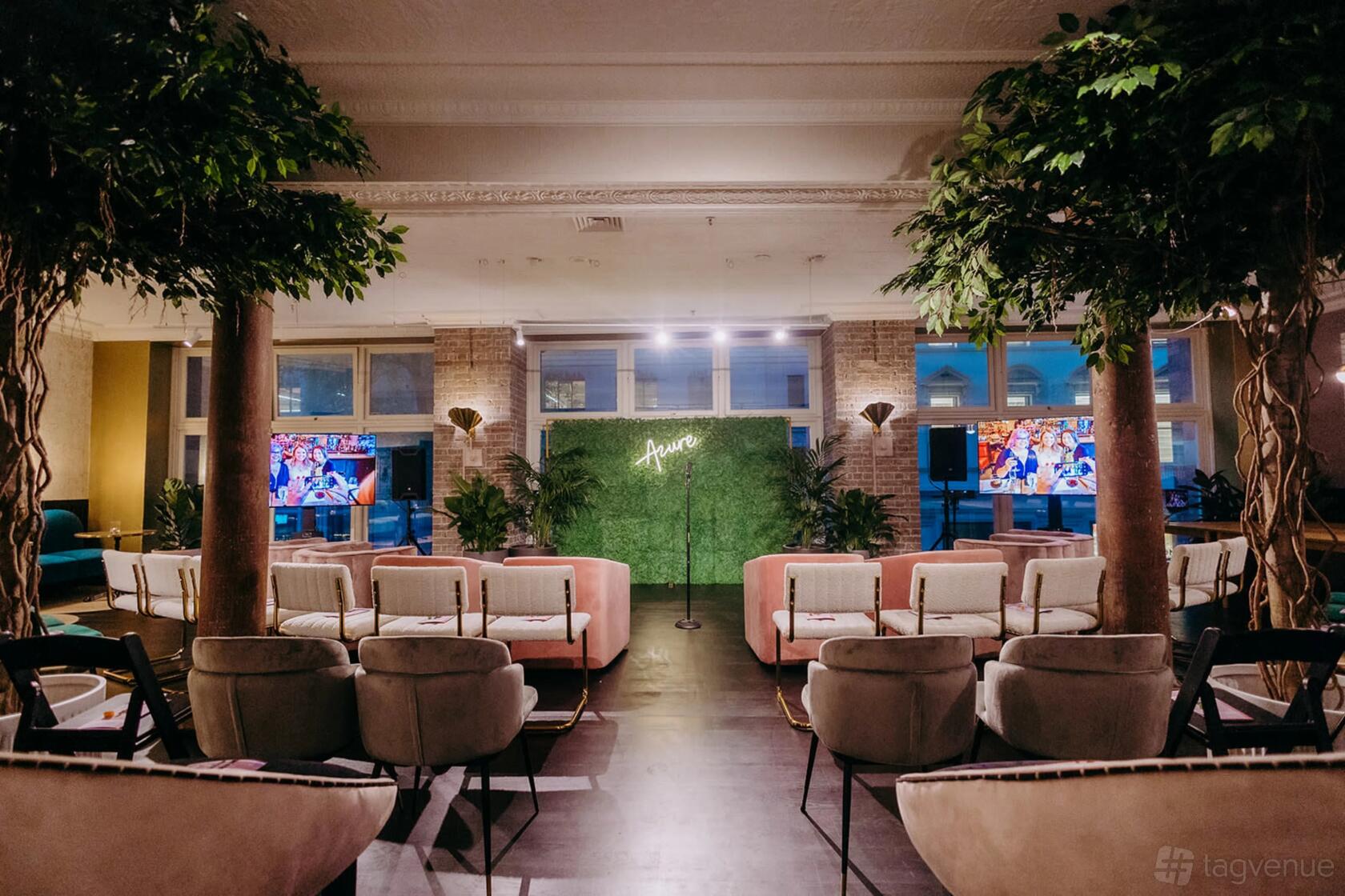 A community centre with indoor trees, velvet chairs, and a green backdrop with neon signage at Business Chicks.