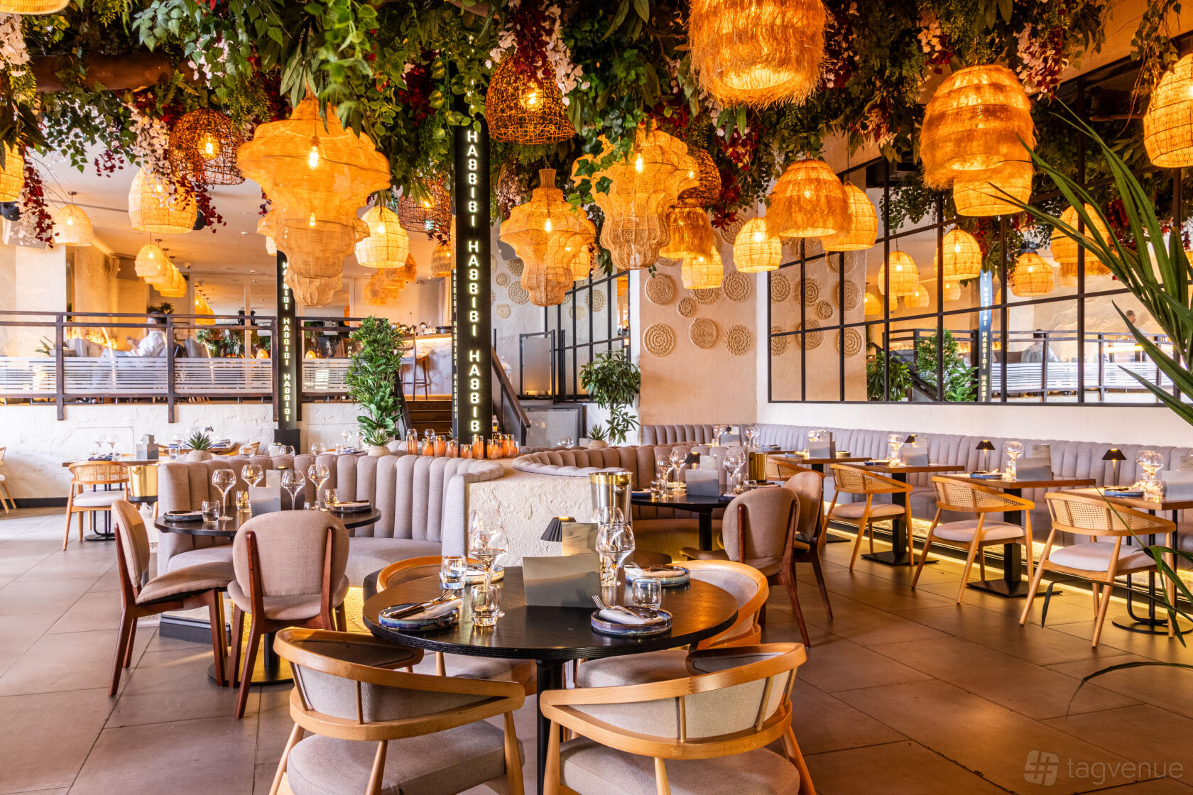 A rooftop restaurant with wicker pendant lights, hanging greenery, and round tables set for dining at Habbibi Leeds.
