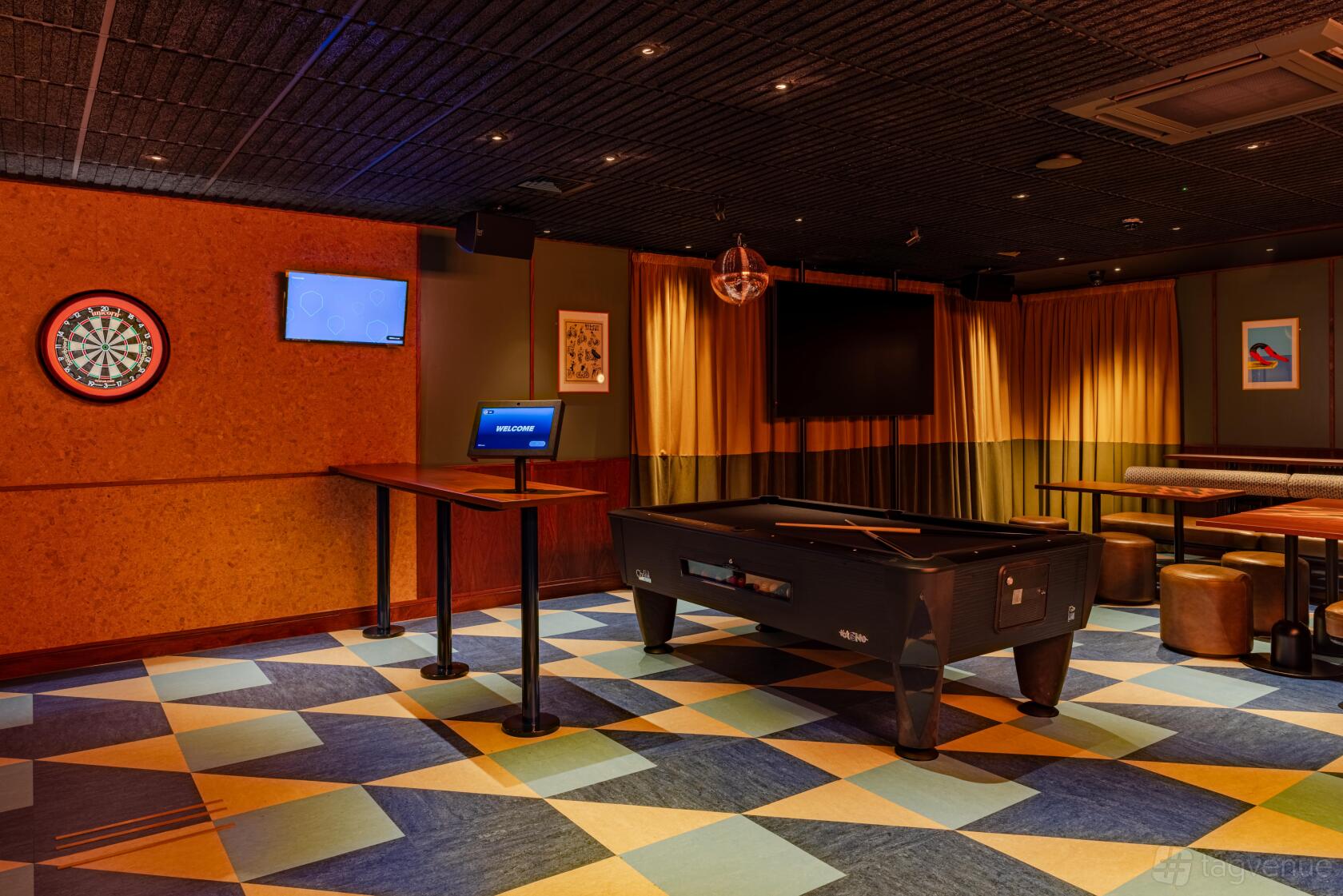 An event space in a bar with a pool table, dartboard, geometric patterned flooring, and lounge seating at KERB Social Club Spitalfields.