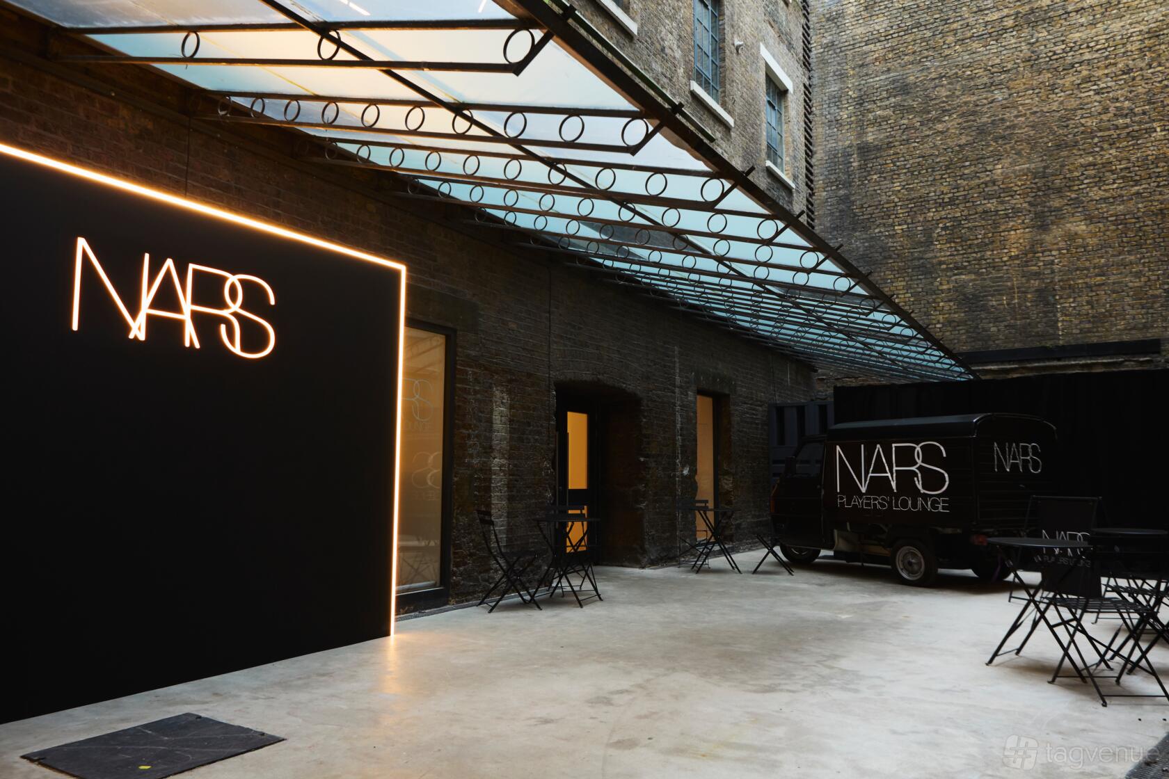 A gallery courtyard with glass canopy, exposed brick walls, and black folding chairs at The Stables (Covent Garden).