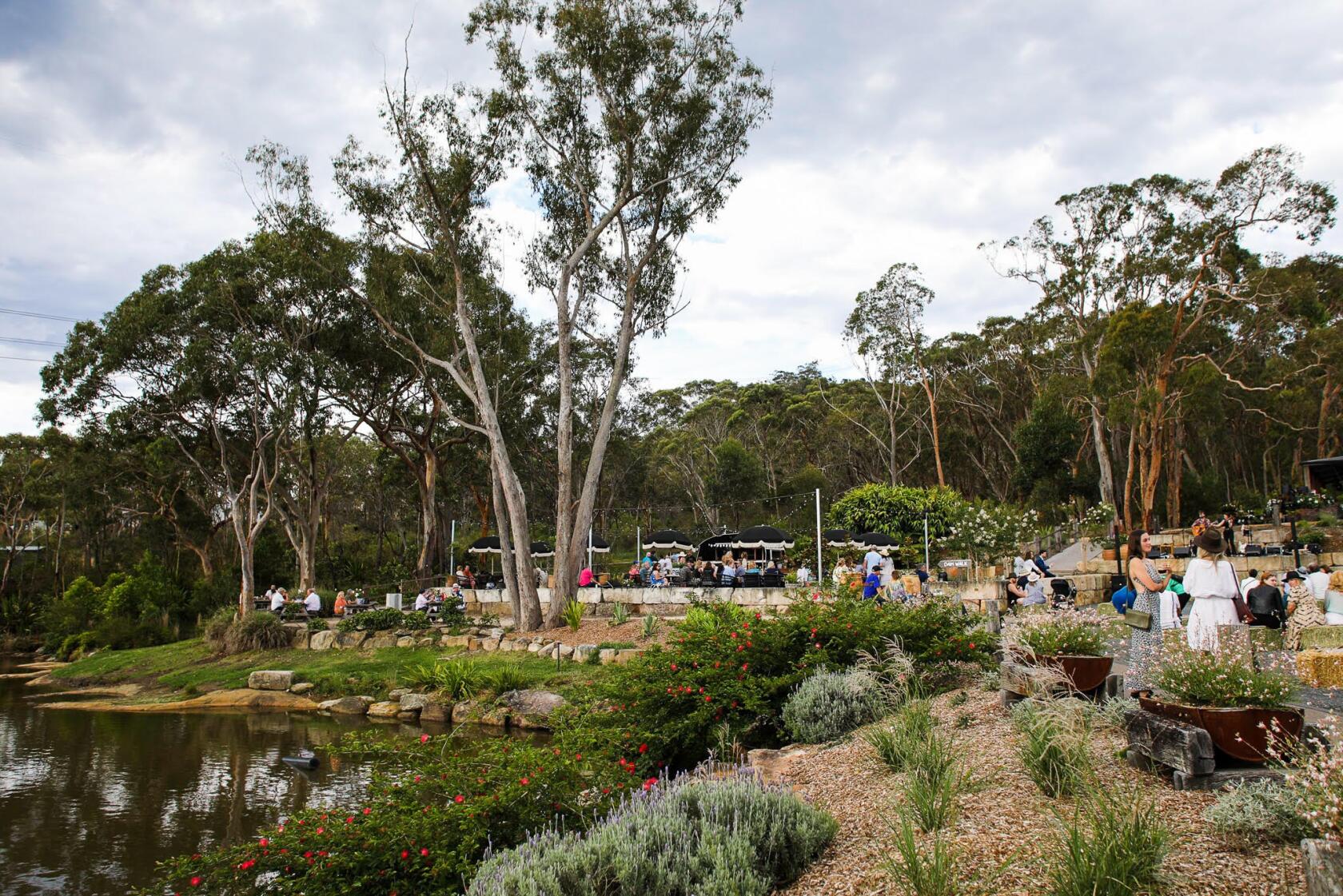An outdoor space with lakeside seating, shaded tables, and landscaped gardens at Saddles Mount White.