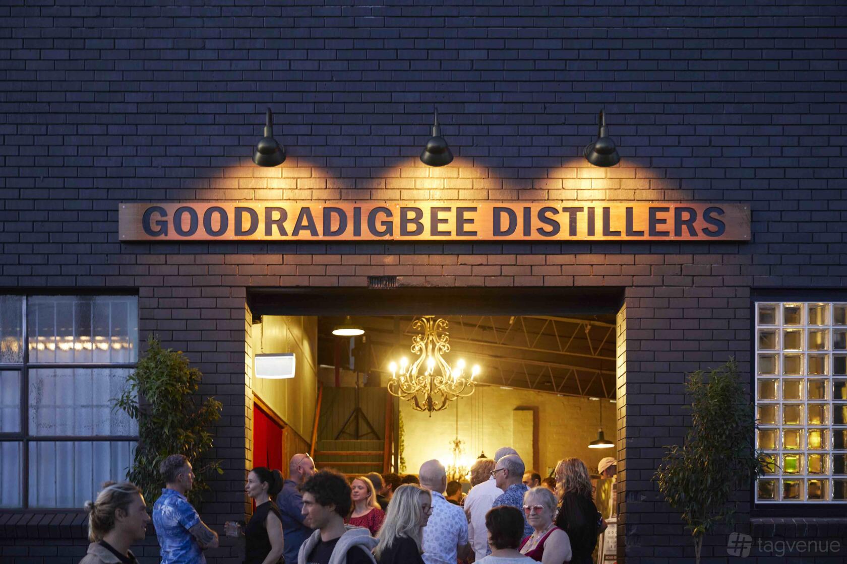 A pub entrance with large industrial doors and a crowd gathered under a glowing chandelier at Goodradigbee Distillers.