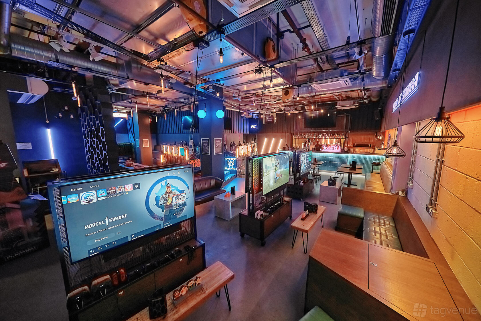 A bar with exposed ceilings, neon accents, gaming stations, and a long wooden bar at Platform Shoreditch.