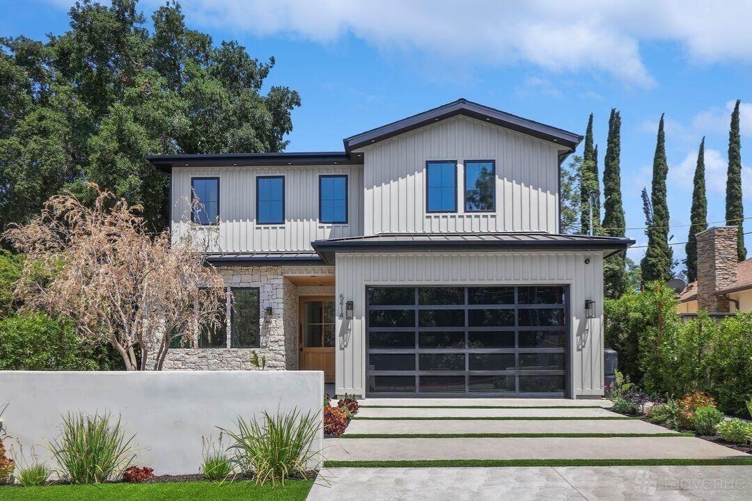 A house with a modern facade, large glass garage door, stone accents, and landscaped front yard at The Aura Three.