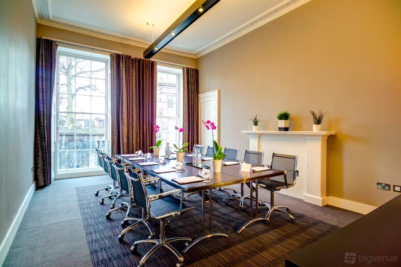 A meeting room with large windows, a long conference table, black chairs, and potted orchids at Apex Waterloo Place Hotel.