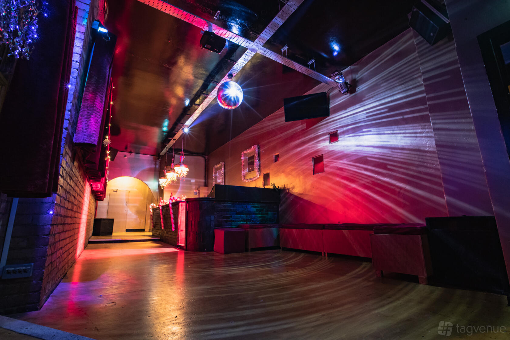 An upstairs event space with a disco ball, colorful lighting effects, and long couches at The Clapham Grand.