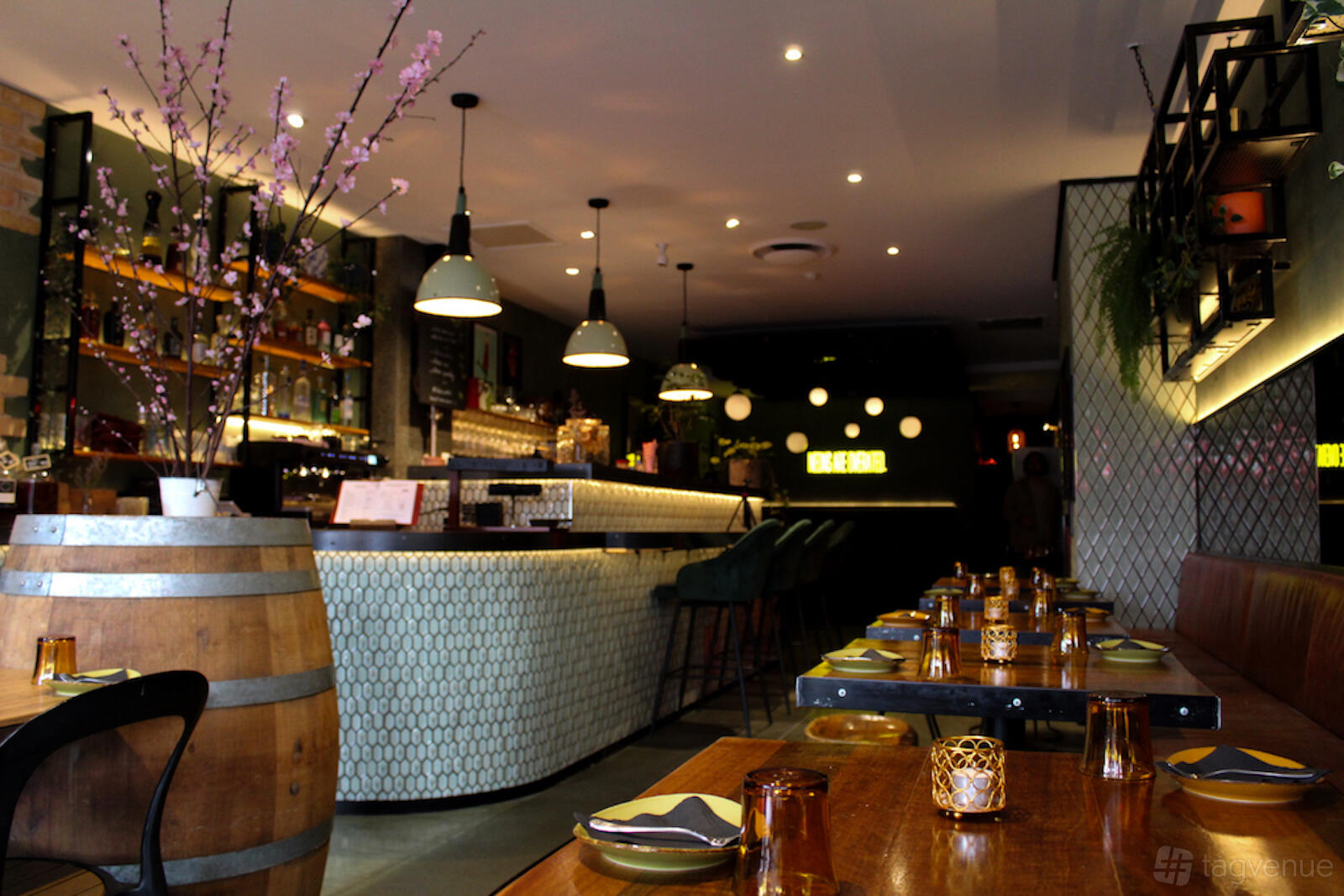 A restaurant with pendant lighting, a marble-tiled bar, and wooden tables set for dining at Lucien Bar.
