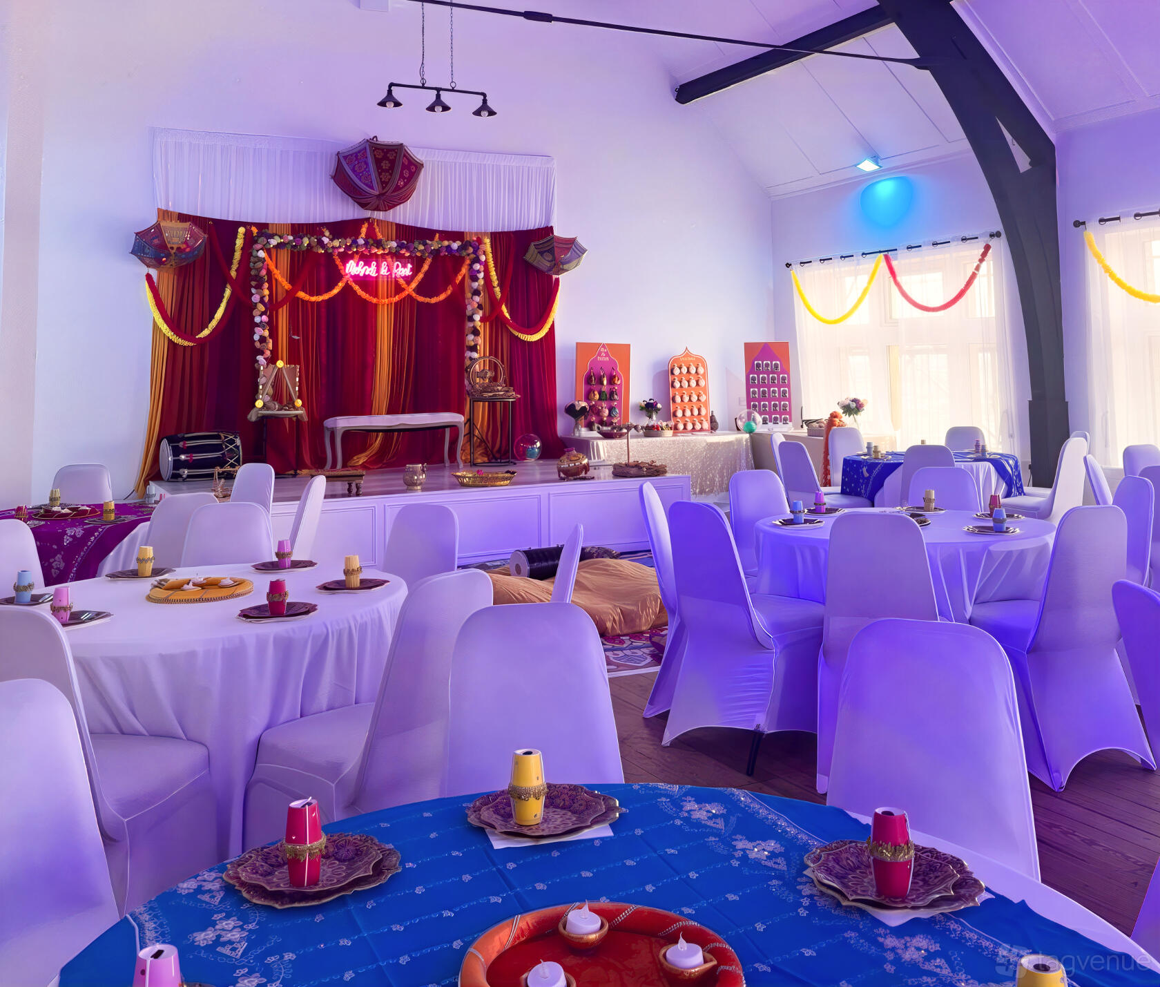 An event venue with round tables covered in white linens, colorful drapery, and a stage at Signature Suites.