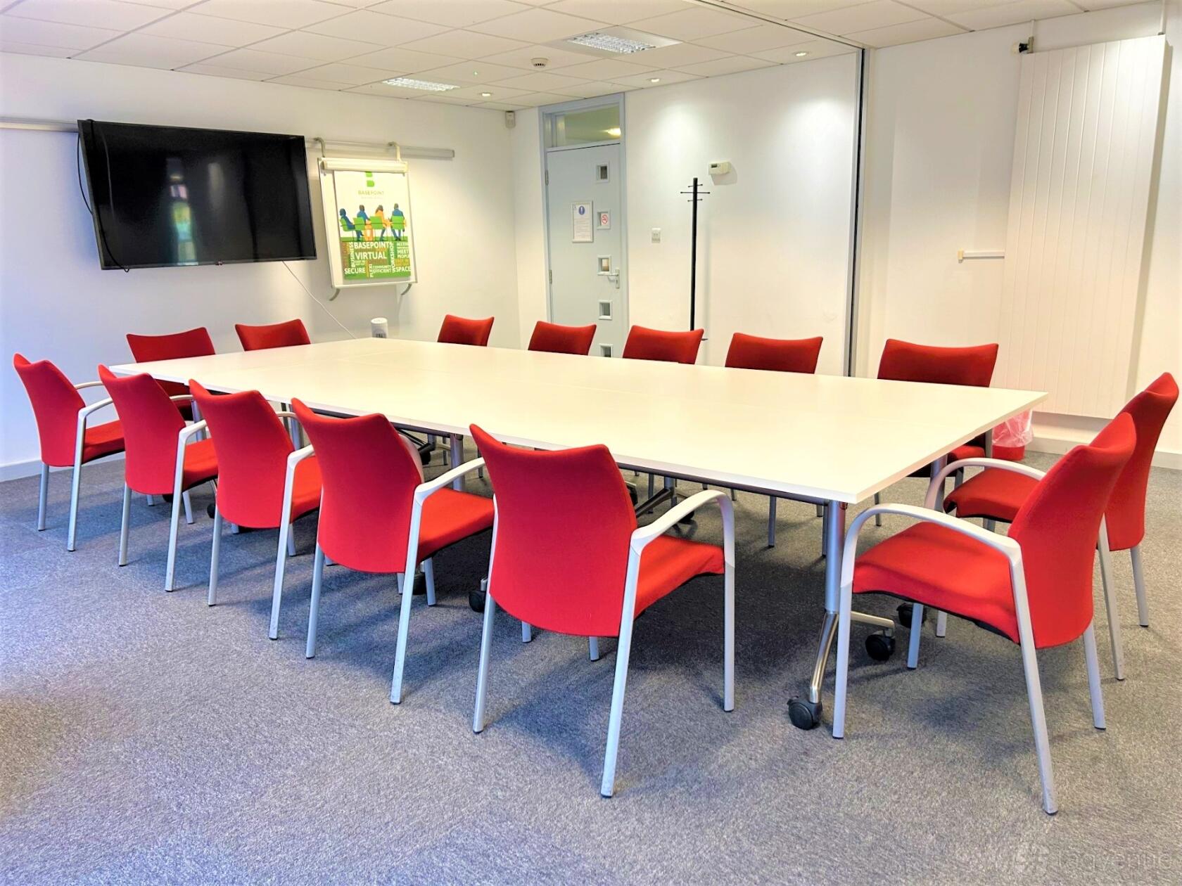 A boardroom with a long white conference table, red chairs, wall-mounted TV, and grey carpet at Basepoint - Southampton, Andersons Road.