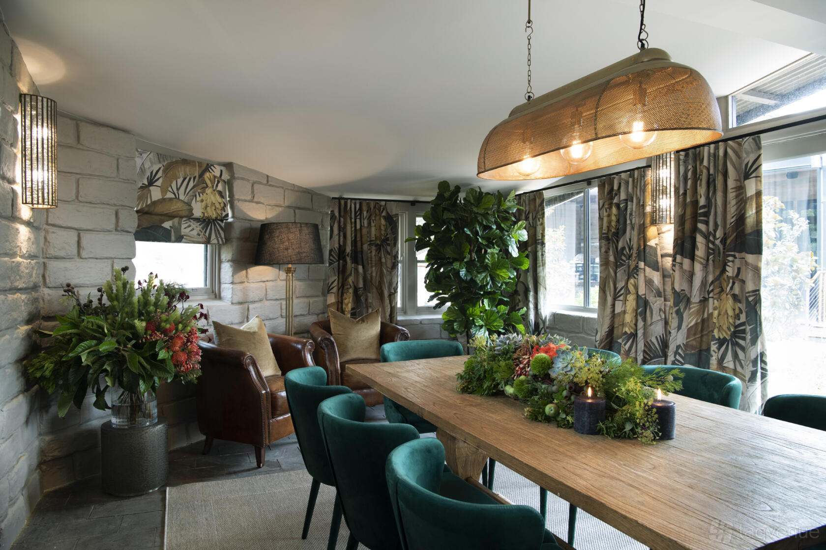 A restaurant dining room with a rustic wooden table, green velvet chairs, and large windows at Saddles Mount White.
