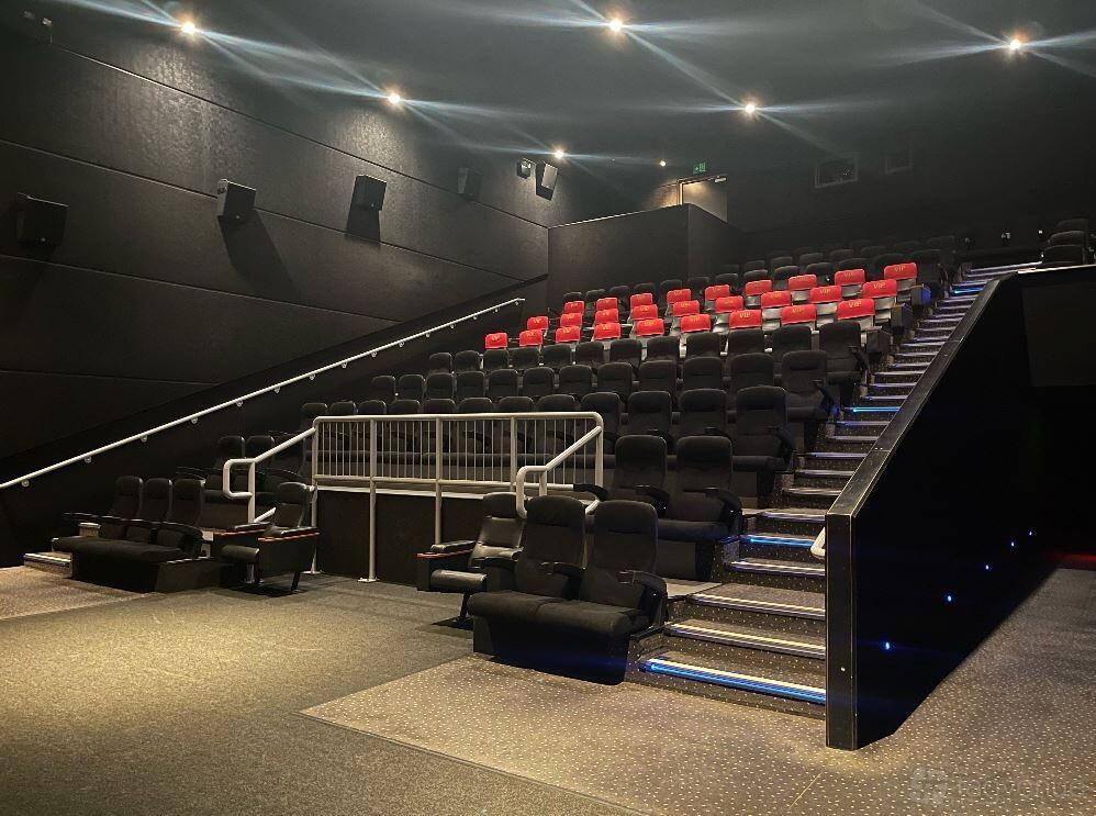 A screening room with tiered rows of black recliner seats and subtle aisle lighting at Vue Westfield London (White City).