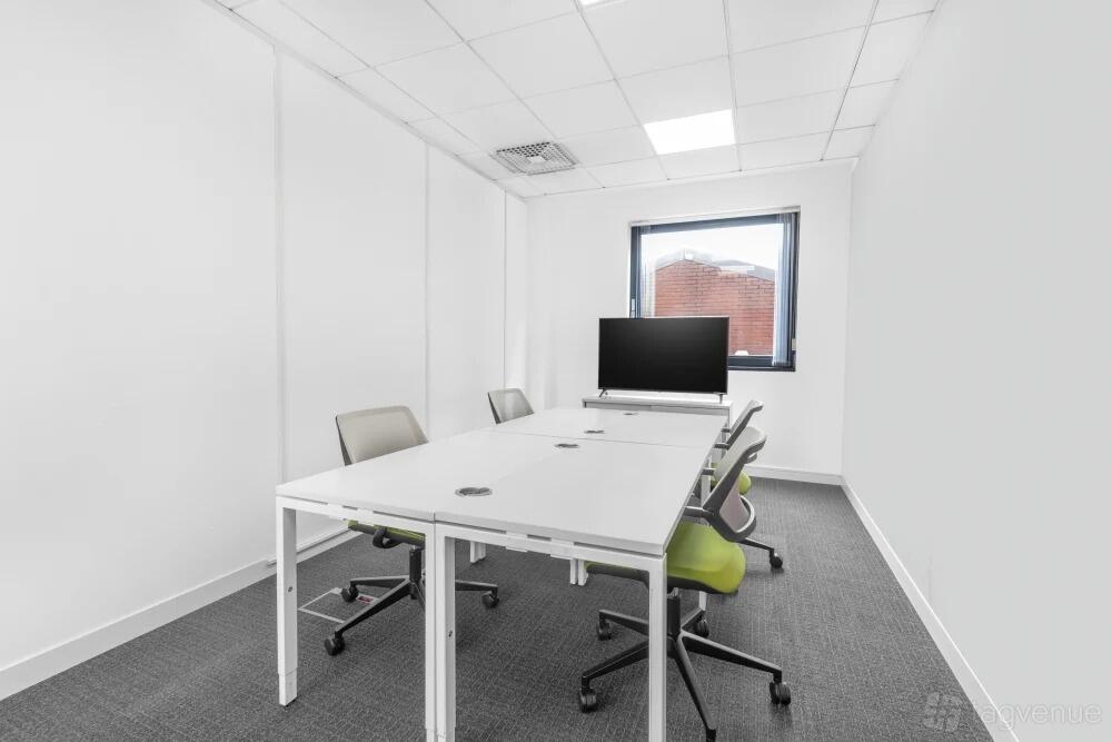 A meeting room with a rectangular table, office chairs, and a wall-mounted screen at Regus – Belfast City Centre.