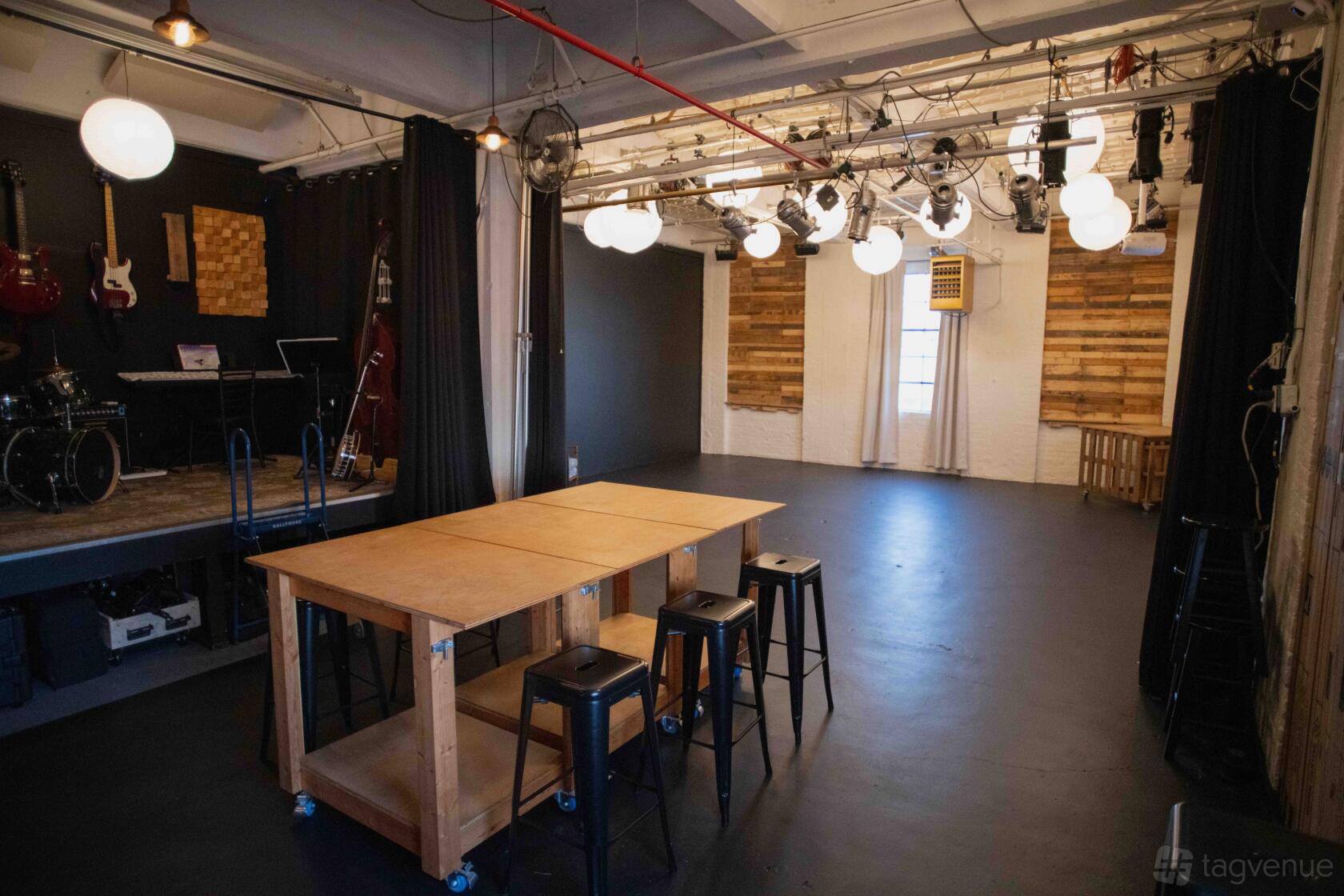 A production studio with black floors, wooden tables, stage with instruments, and overhead lighting at NLK Studio.