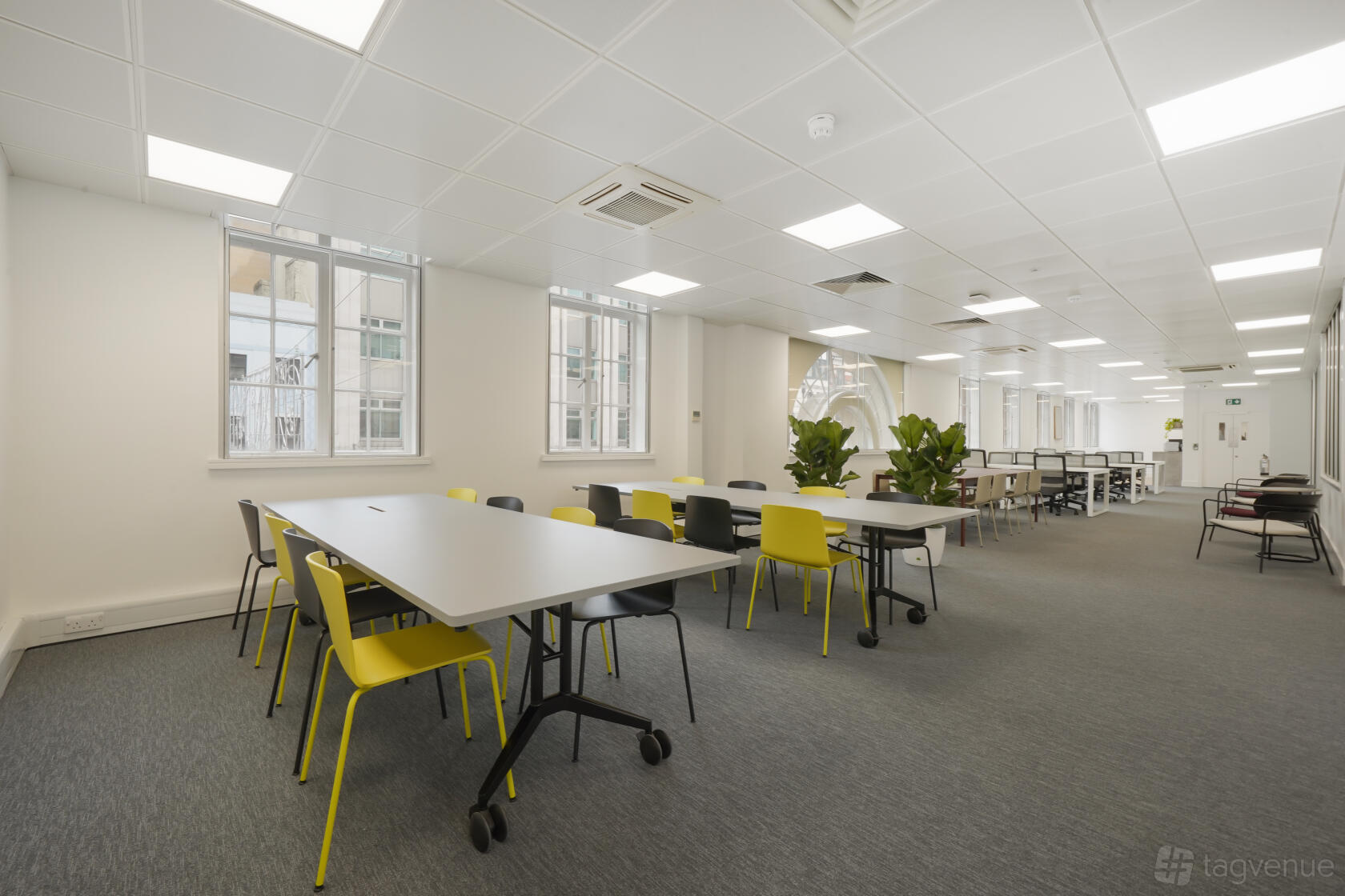 An event venue with flexible tables, mixed colorful chairs, and large windows at Oasis.