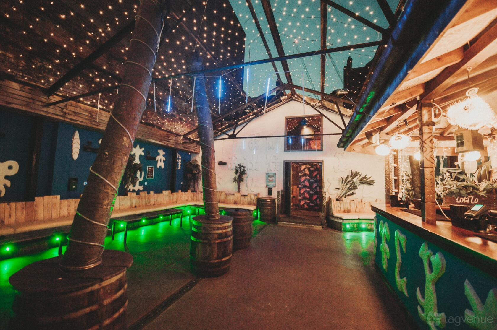 A nightclub terrace with palm trees, barrel tables, string lights, and tropical decor at Lola Lo Reading.