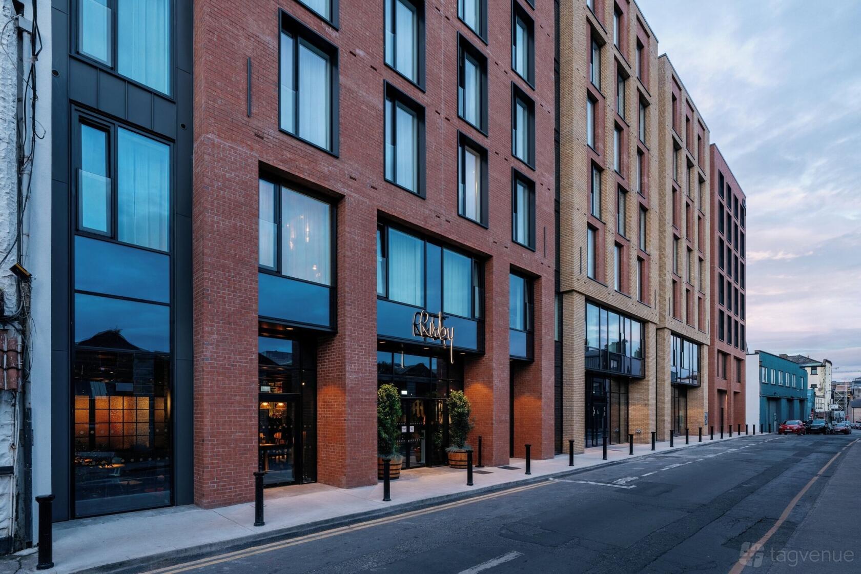 A hotel with a red brick facade, large floor-to-ceiling windows, and a street entrance at Ruby Molly Hotel & Bar.