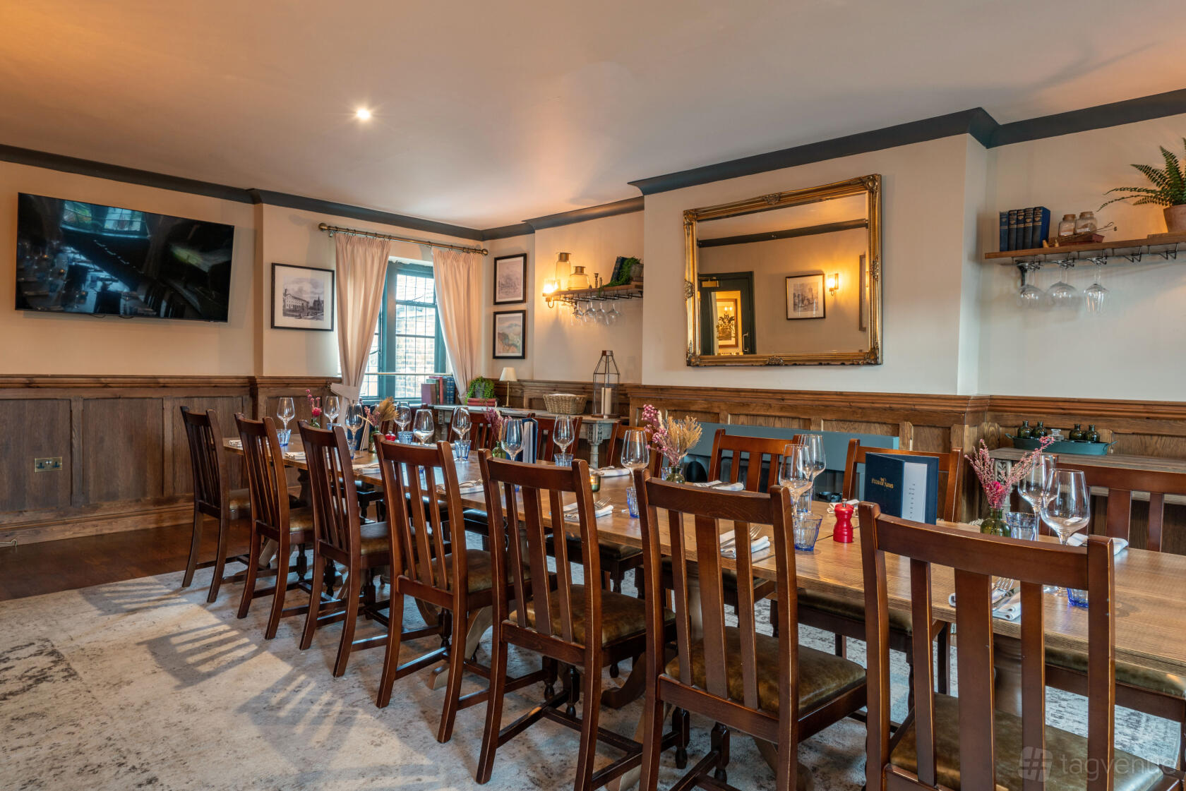 A function room in a pub with a long wooden table, wine glasses, framed art, and a large mirror at The Fulham Arms.