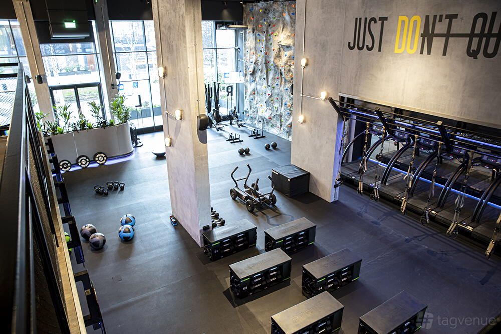 A fitness studio with treadmills lined along one wall, free weights, kettlebells, and a rock climbing wall at RUMBLE.