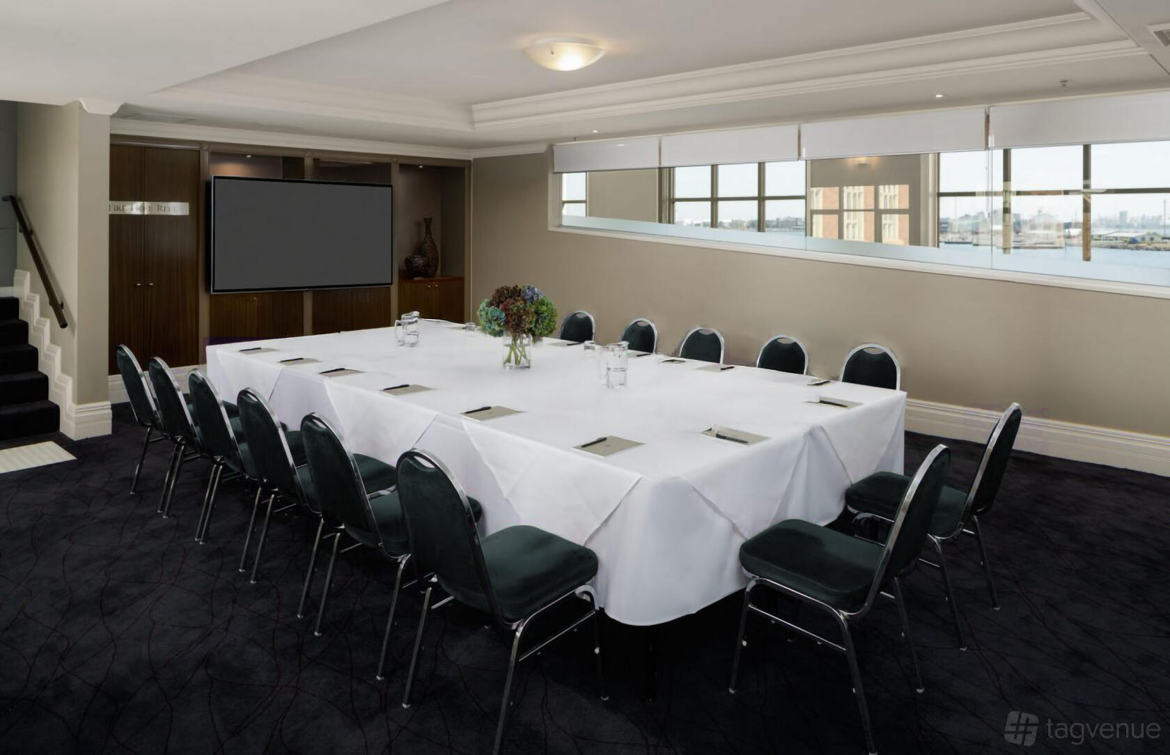 An event space with a U-shaped table arrangement, white linens, and large windows at Rydges Newcastle.